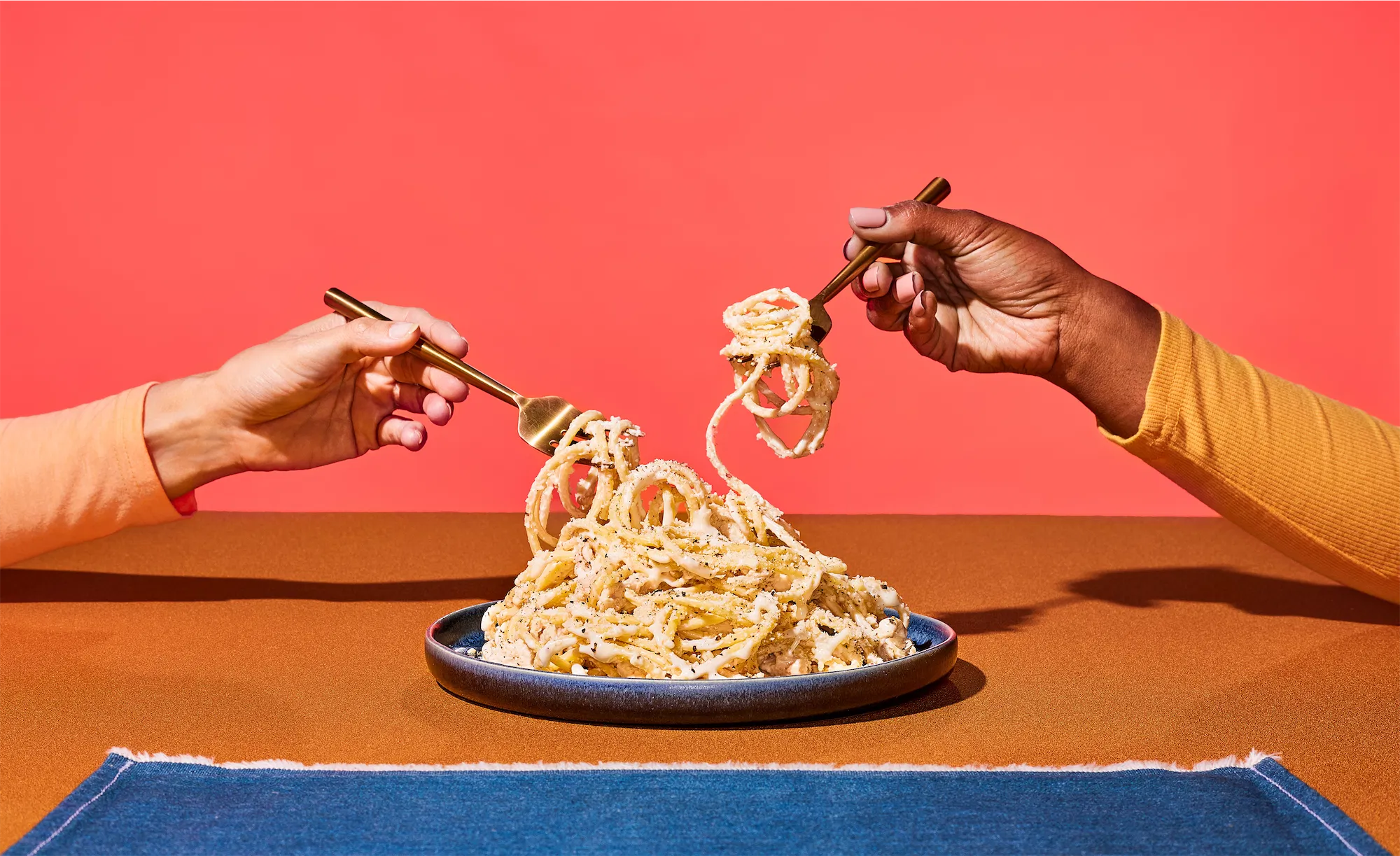 two hands swirling pasta on forks above plate of spaghetti
