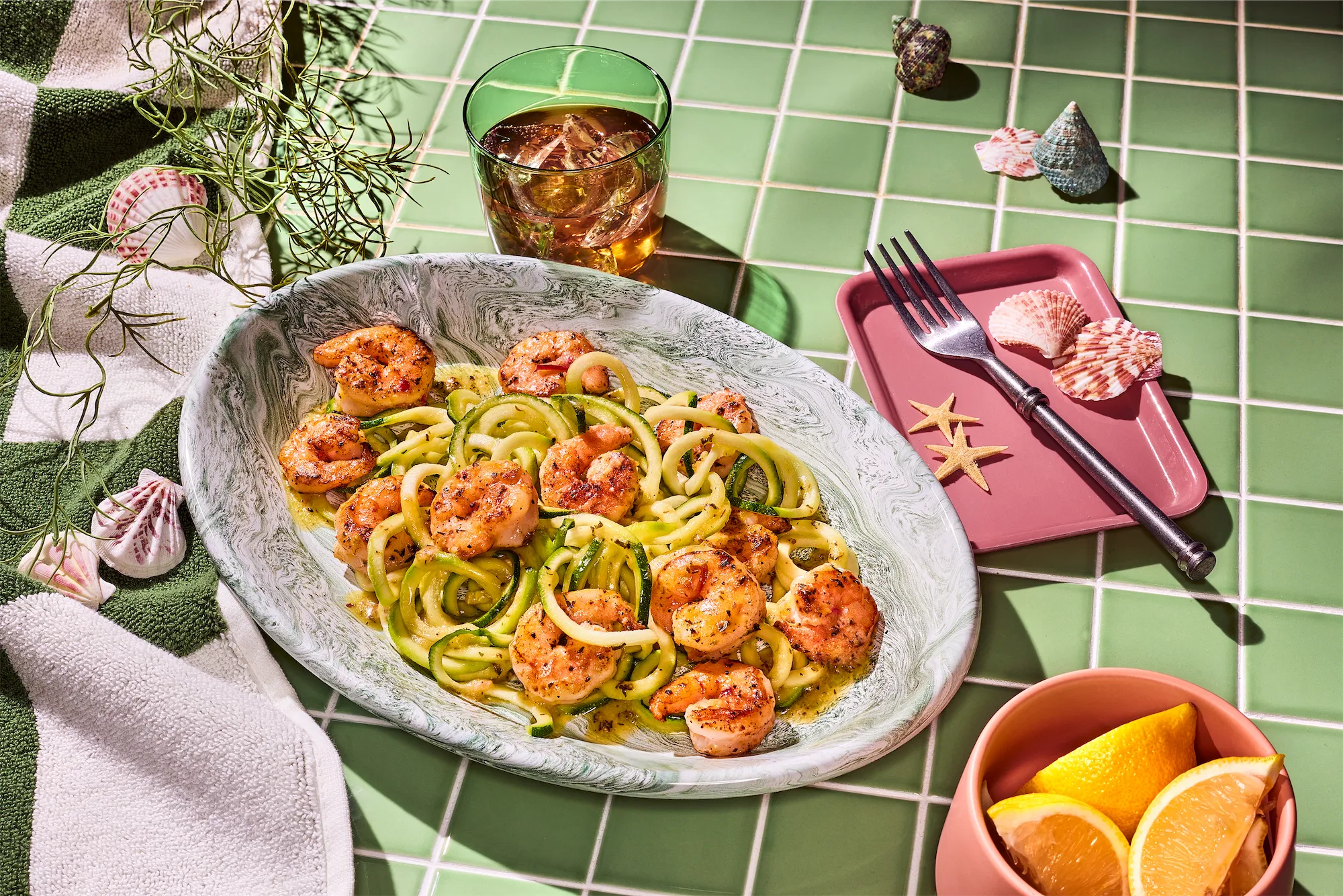 pescanova brand recipe of shrimp with zucchini noodles and fresh lemon wedges in a nautical themed scene on green tile surface