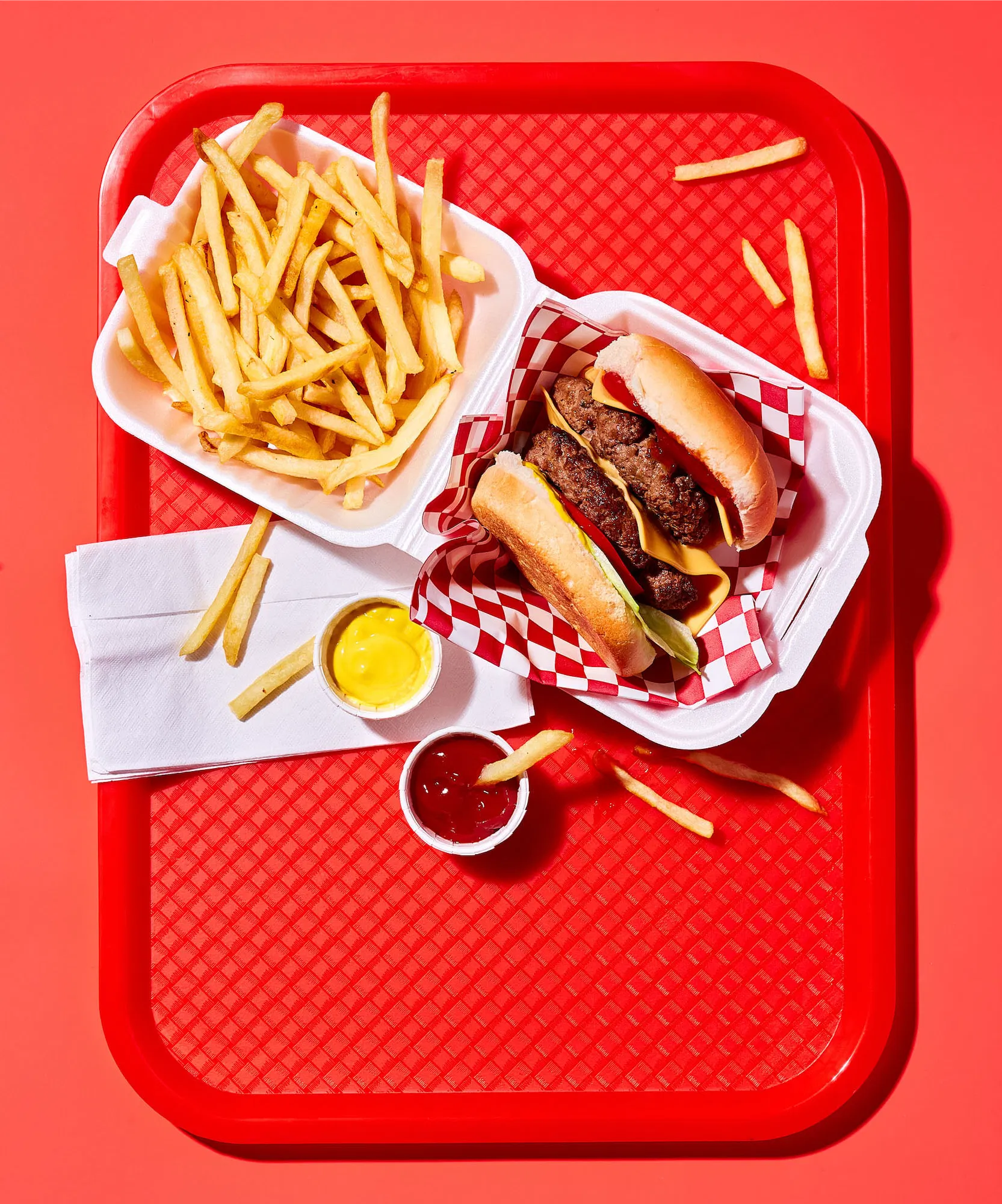 a red diner canteen tray showing a burger and fries in a take-out to go box with mustard and ketchup