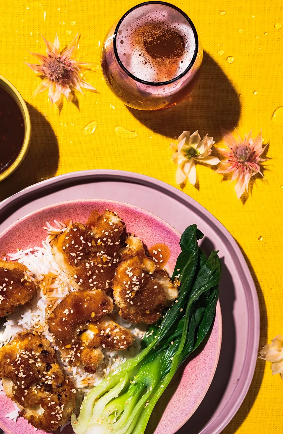 general sao chicken recipe on bed of rice with bok choi and beer on pink plate and yellow background