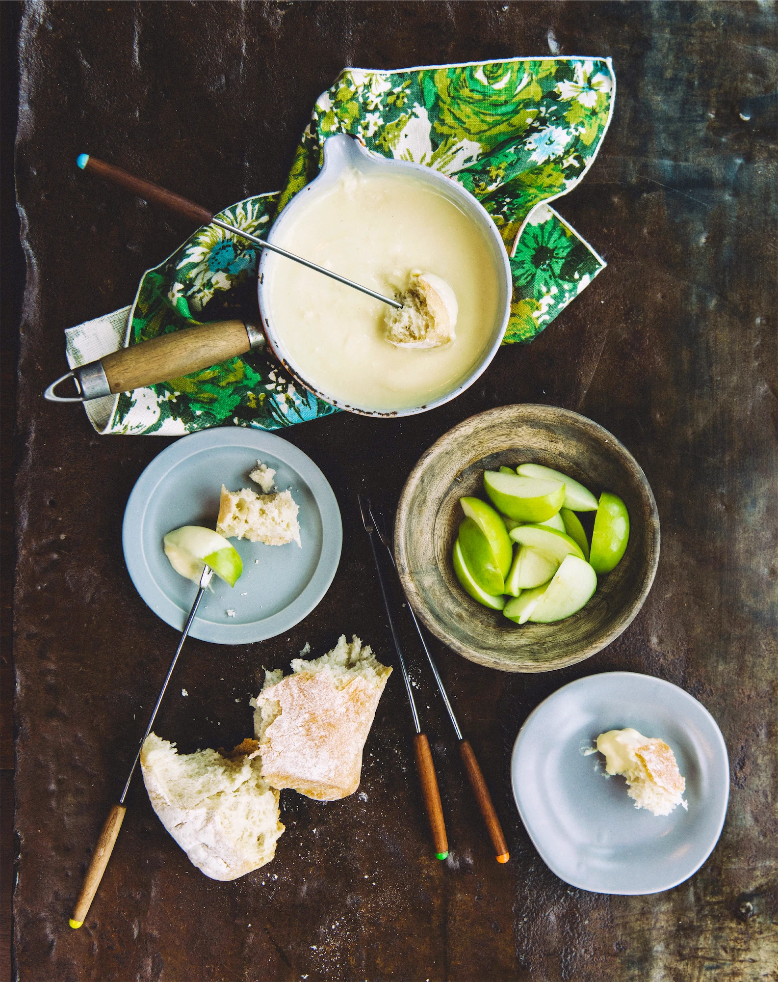 a fondue scene with cheesy sauce and fresh cut apples on a rustic wood surface