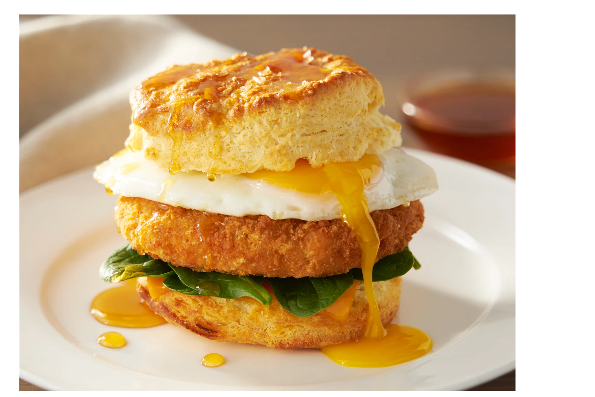 breaded patty fresh baby spinach and a fried egg in a biscuit with yolk dripping down the side on a white plate