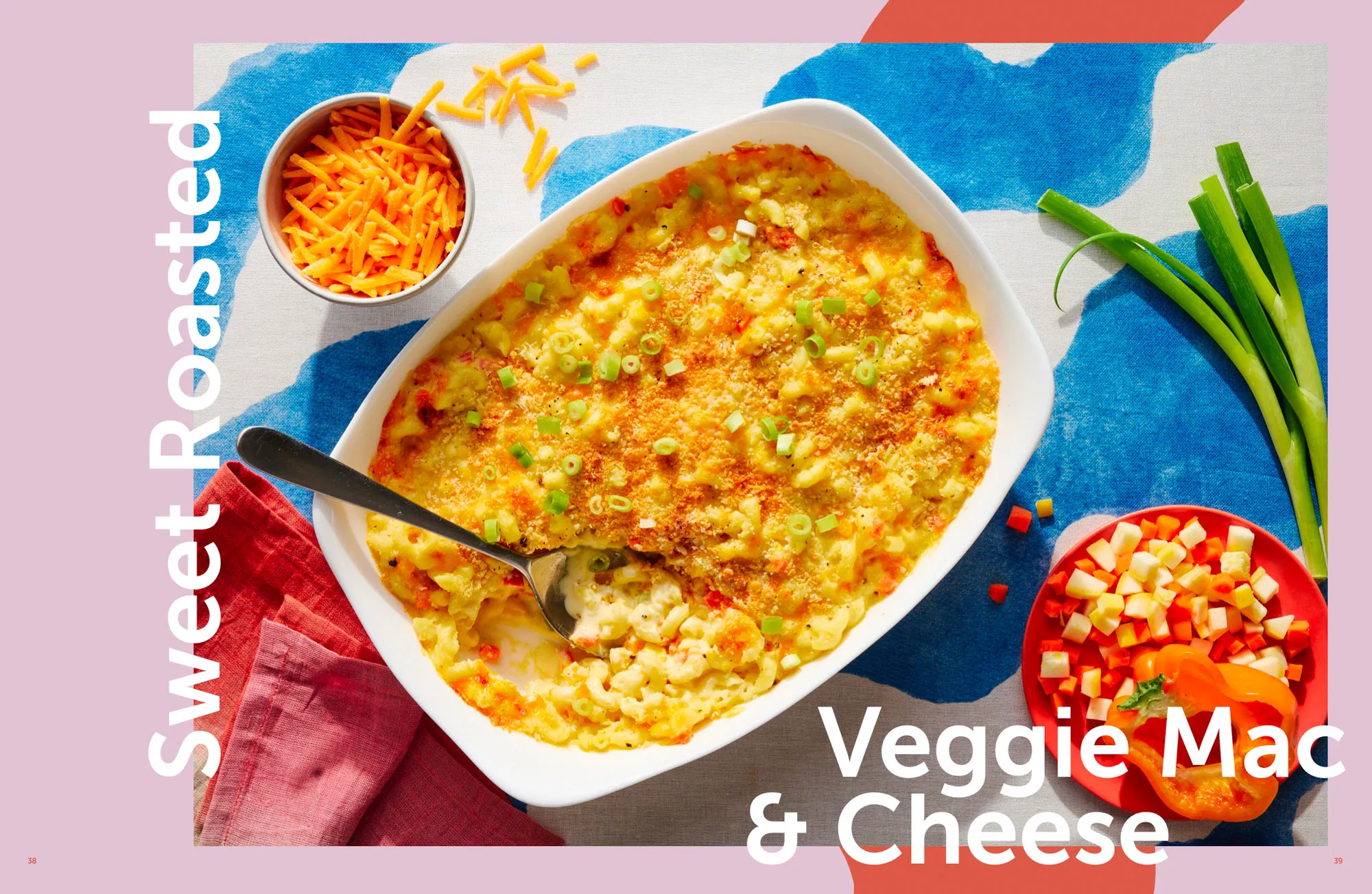 sweet roasted veggie mac and cheese in a white baking dish and a red white and blue surface shredded cheddar and green onions on the side