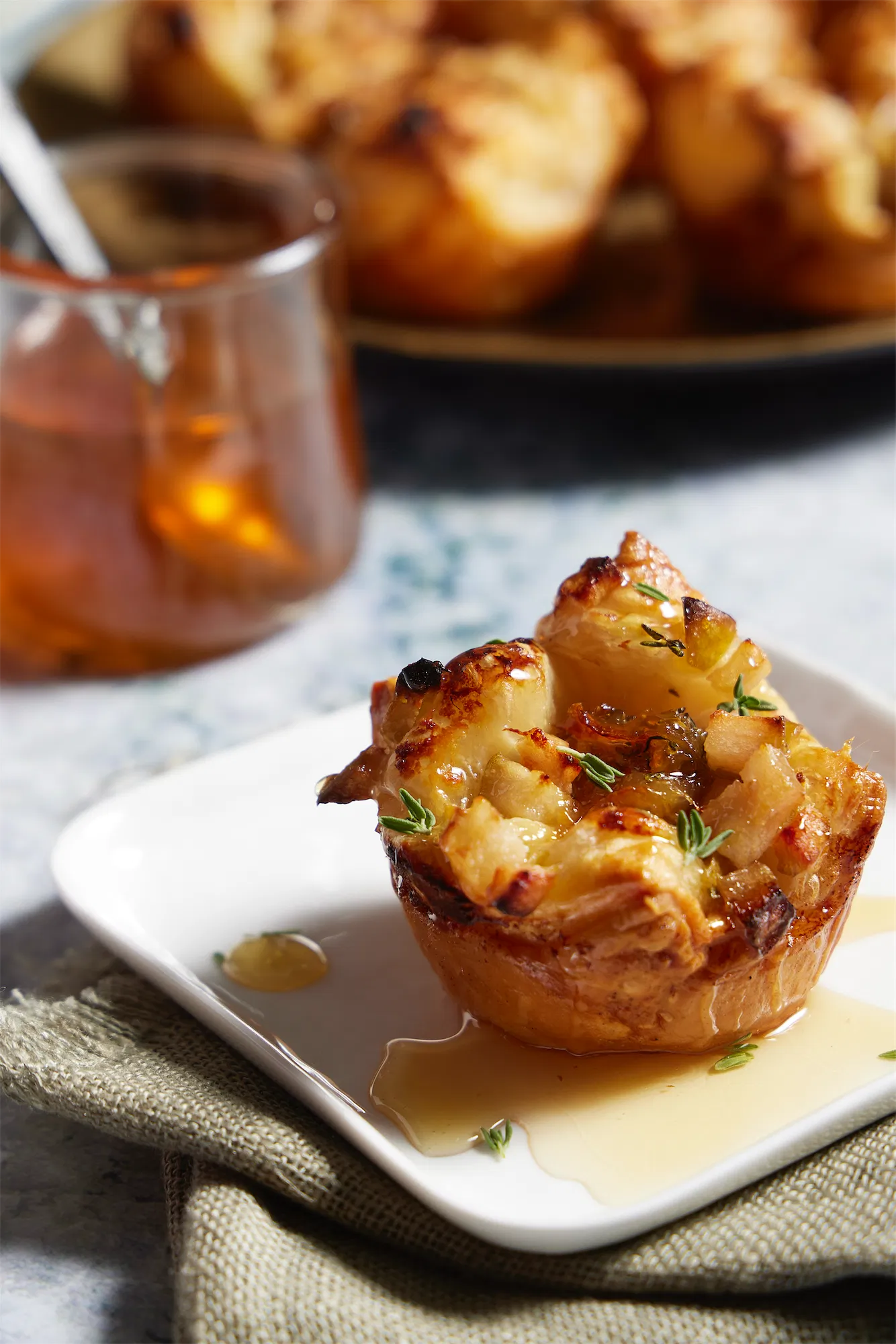 a puff pastry cupcake on a white plate with thyme and honey a jar of honey in background
