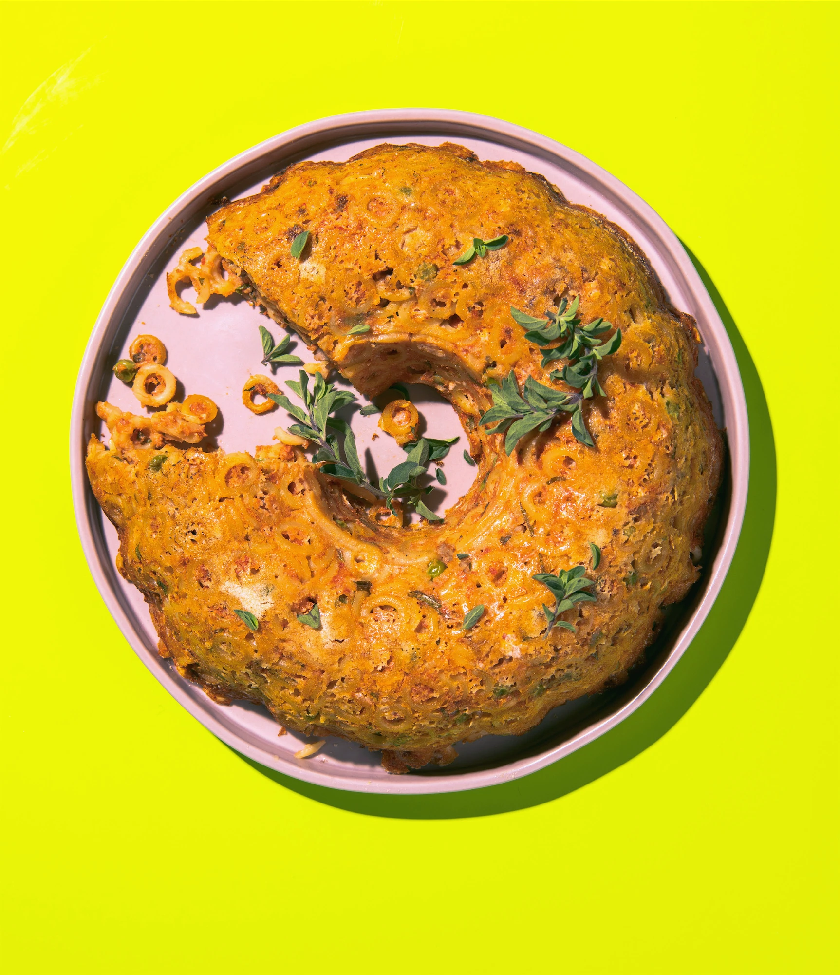 italian noodle recipe made in a bundt pan on a pink plate on cerise background