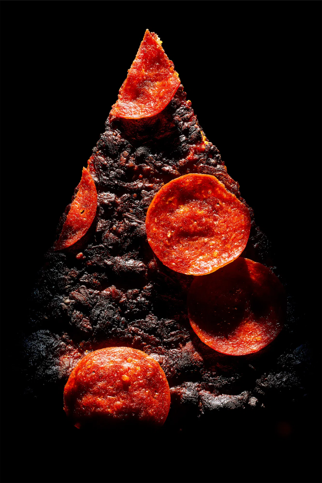a blackened pizza slice with pepperoni on a black background