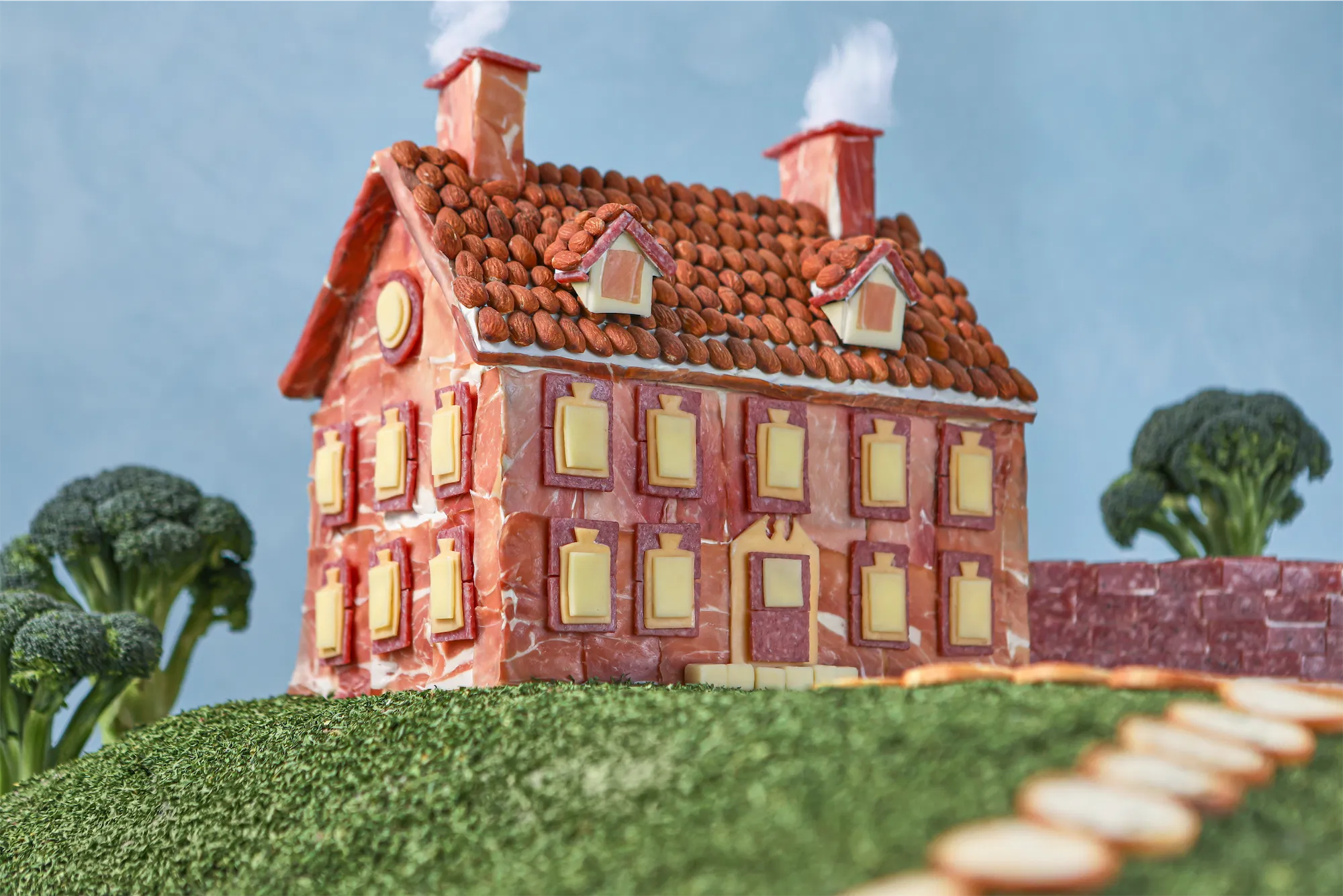 Hillshire farms brand scene of an east cost mansion made entirely of meat and cheese sitting on a green grass hill with broccoli trees