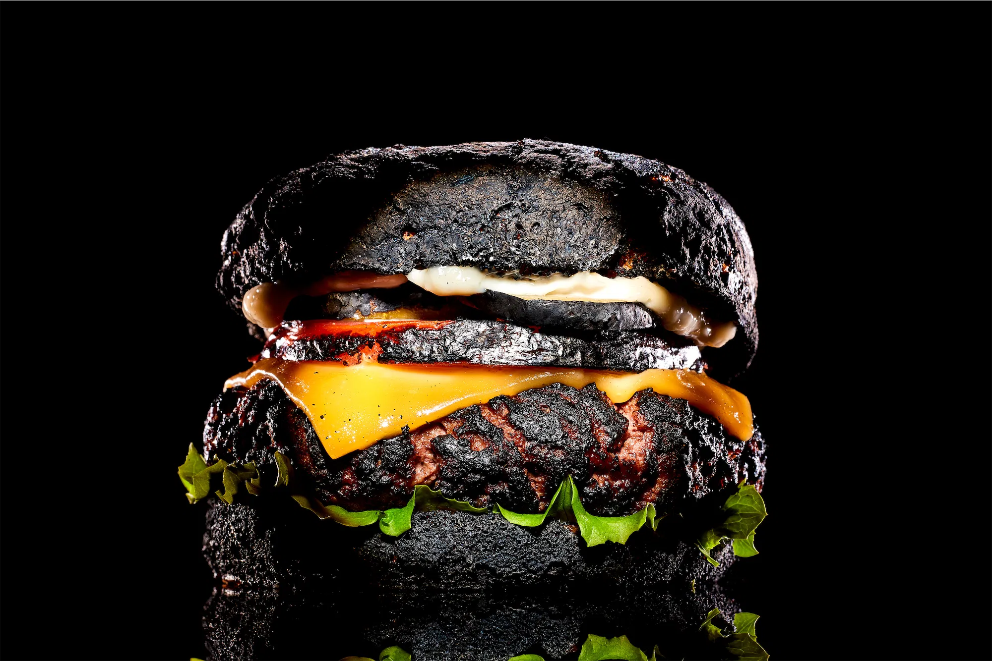 a blackened classic burger with american cheese lettuce and mayo on a black background