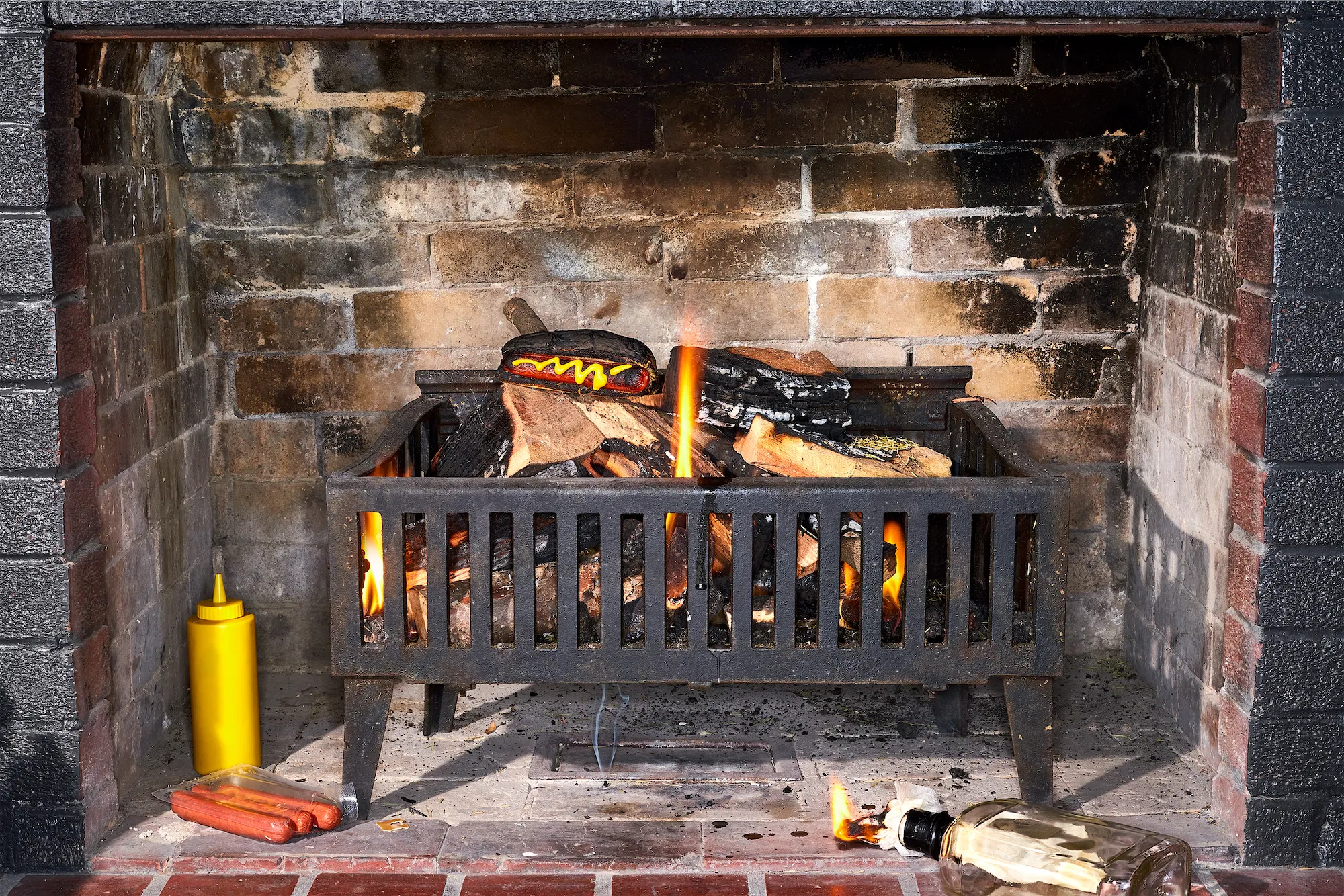 a fireplace scene with hotdogs on the grate and flames burning and a mustard bottle lower left and a molotov cocktail lower right