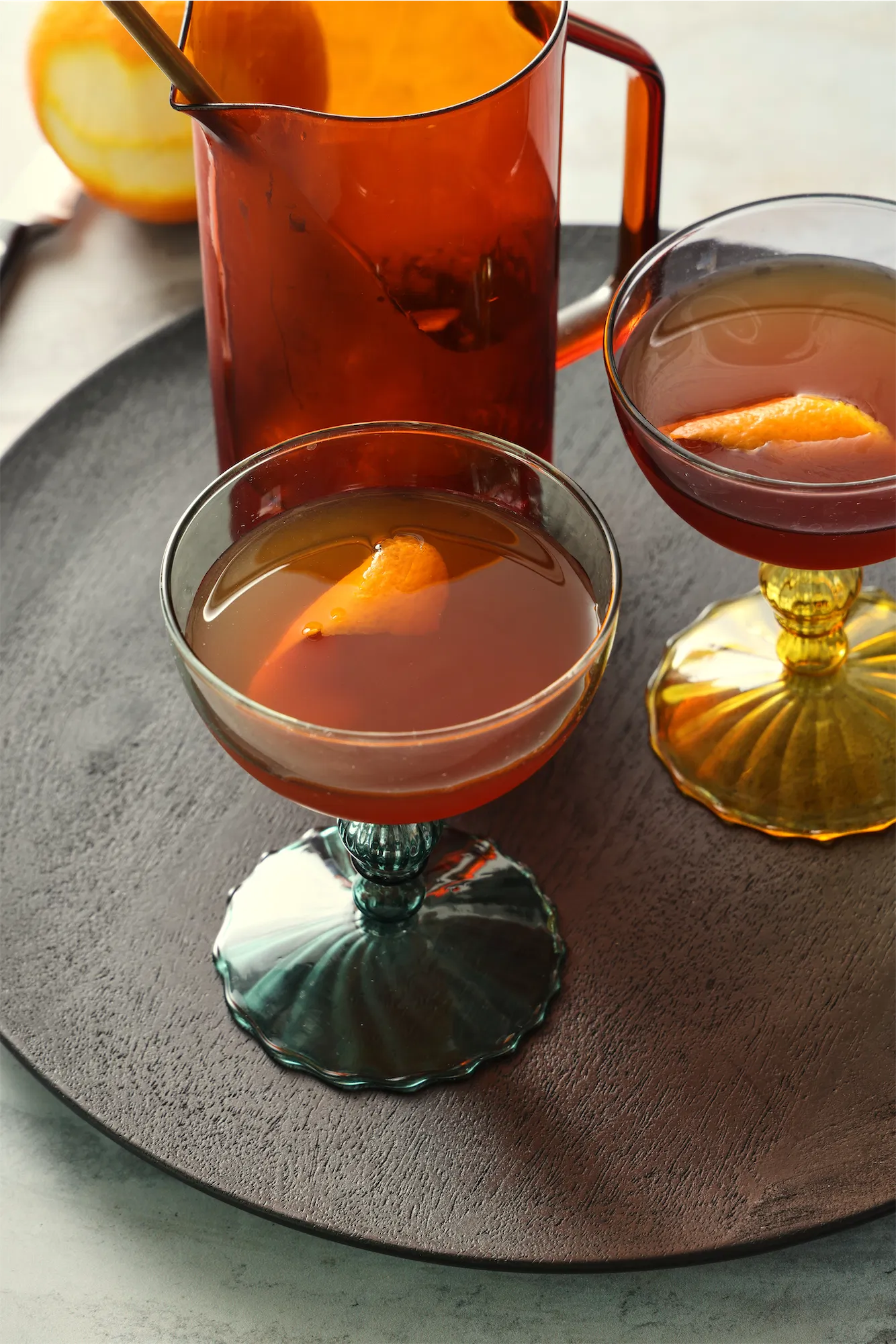 Fall autumn inspired Cynar and Calvados cocktail in a green footed couple with an amber glass pitcher on a wooden tray