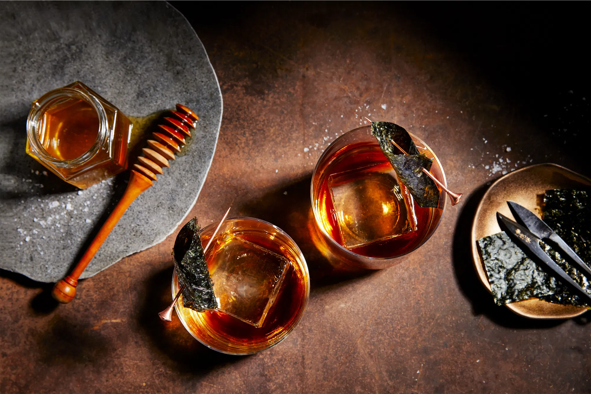pair of old fashioned cocktails in rocks glass with honey twizzler
