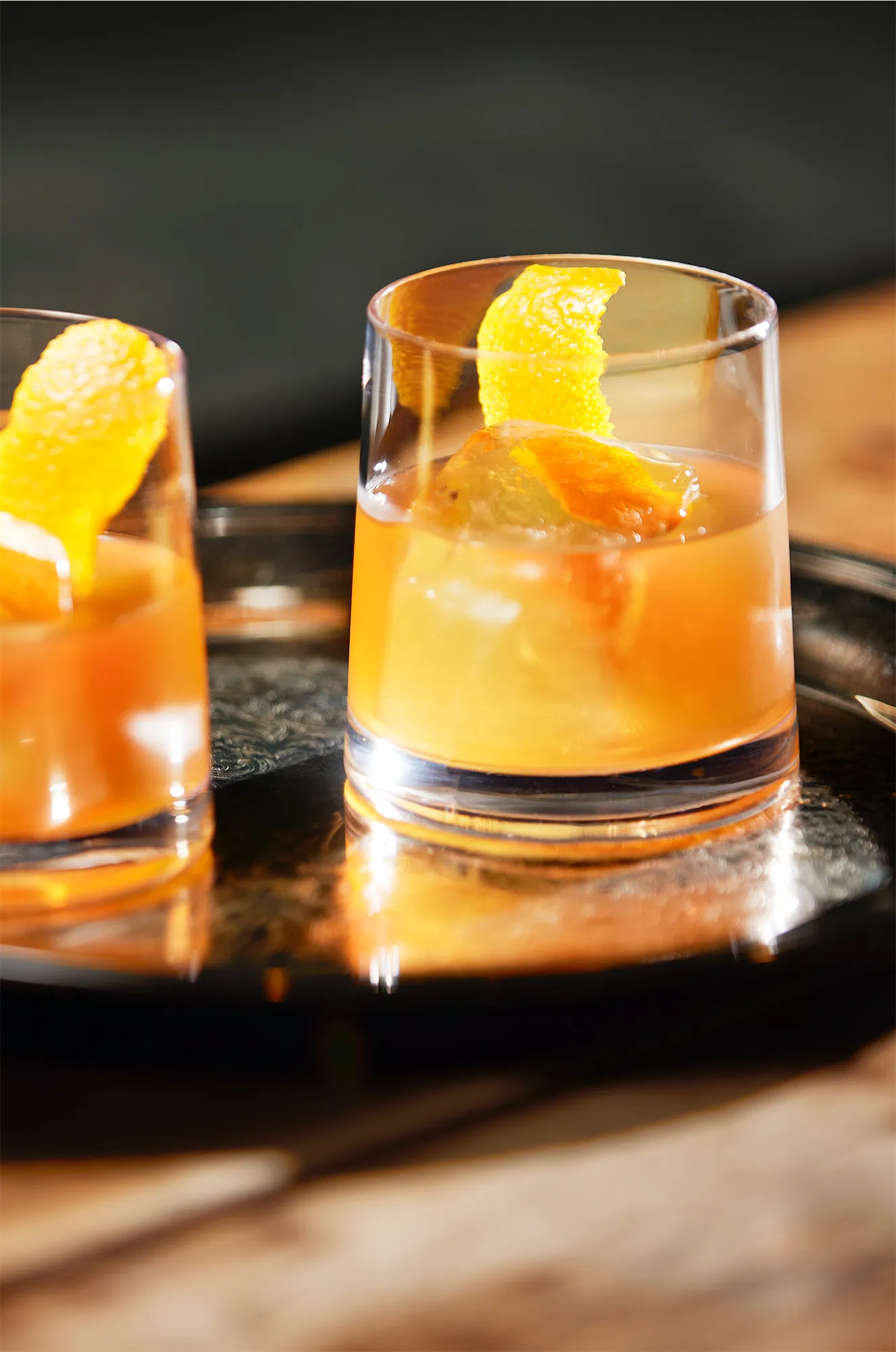 two rocks galsses half filled with coconut fat washed bourbon old fashioned cocktail garnished with orange twist.