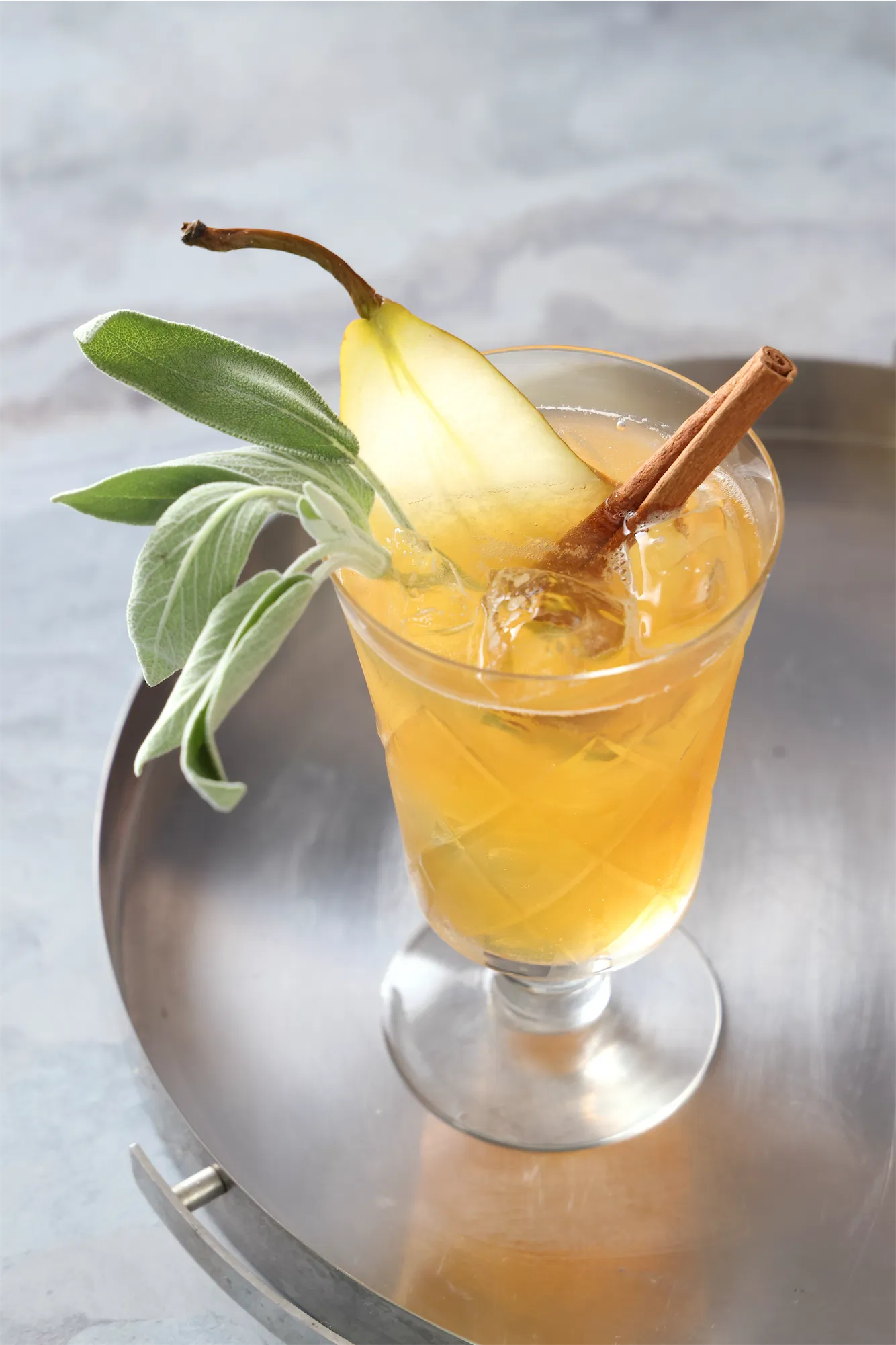 a thanksgiving punch coktail recipe with pear and sage garnish on a round deco stainless tray.