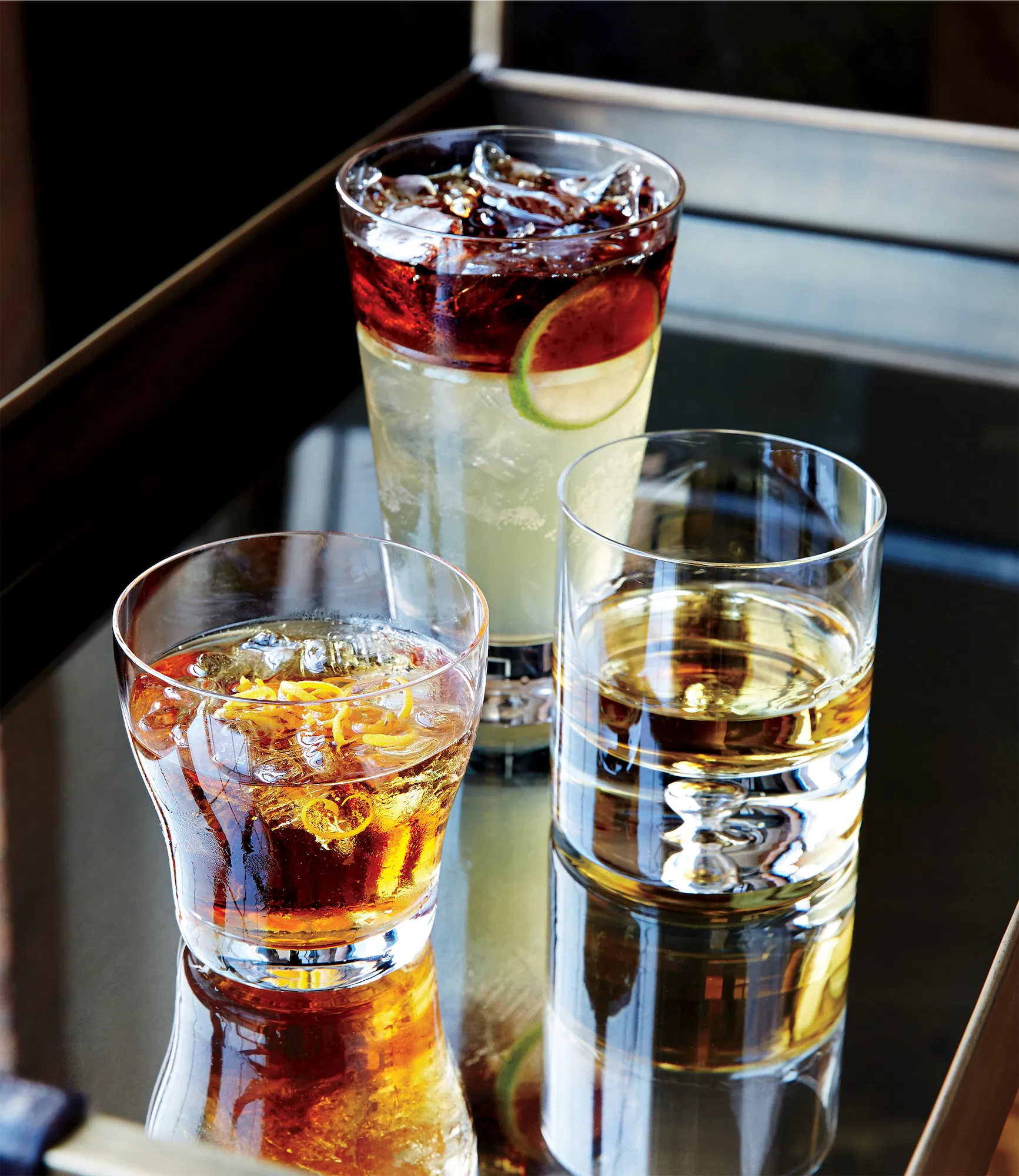 crate and barrel catalog of three different glasses containing cocktails on a reflective surface