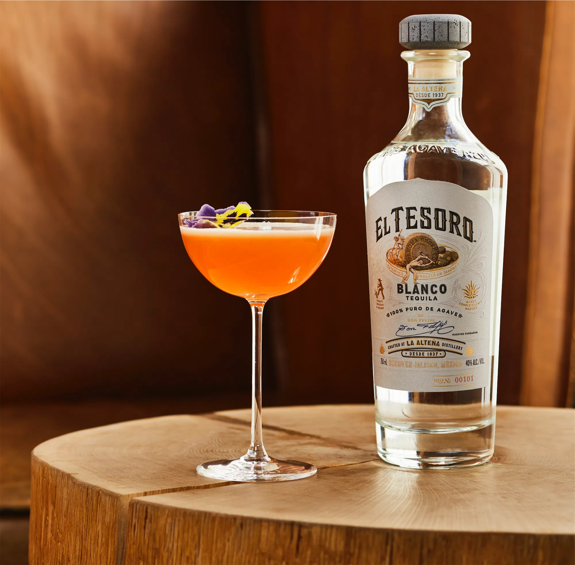 White label brand el tesoro blanco tequila pink cocktail in a coupe on a round wood table