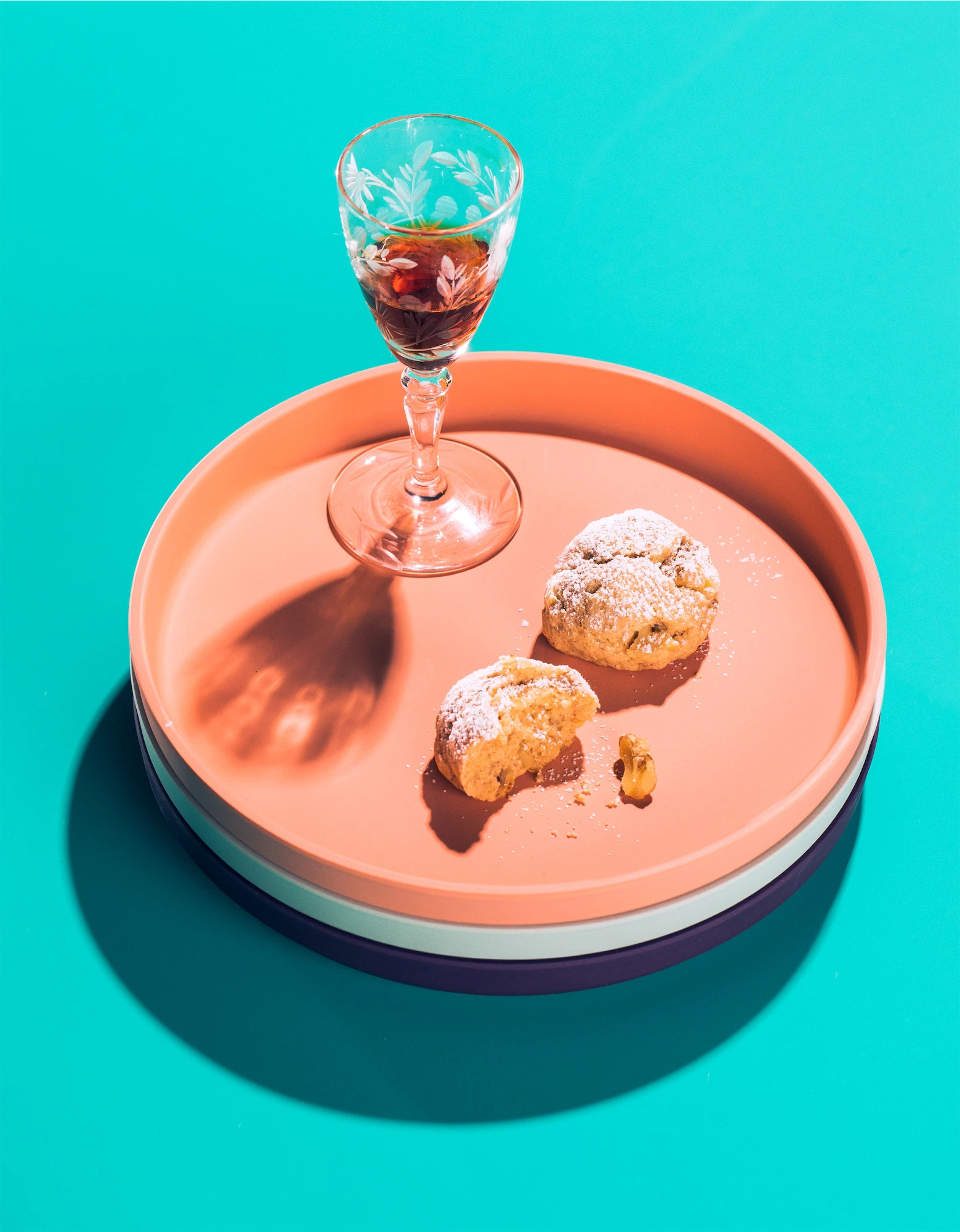 vintage glass of amaro with an italian cookie on a pink plate on teal background