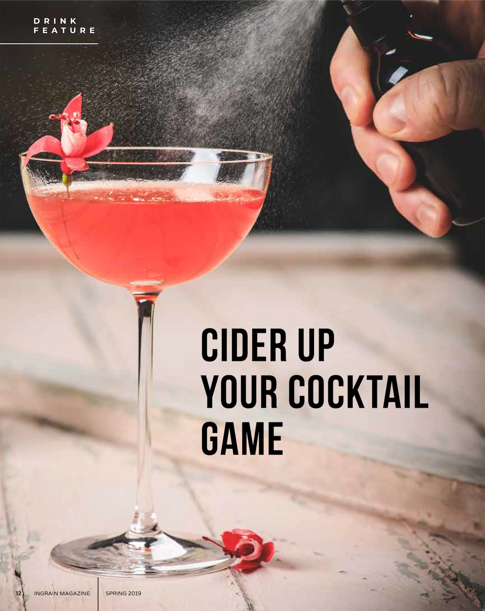 a pink cocktail in a coupe glass with a hand spritzing and a flower garnish