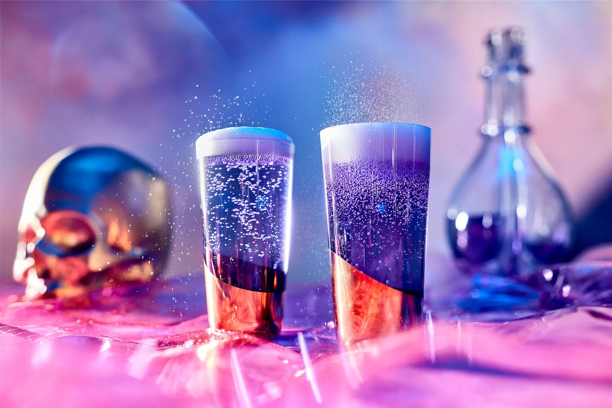 a pair of gold dipped champagne glasses filled with sparkling wine and a gold skull in the background of a dreamy purple and pink cloudy scene