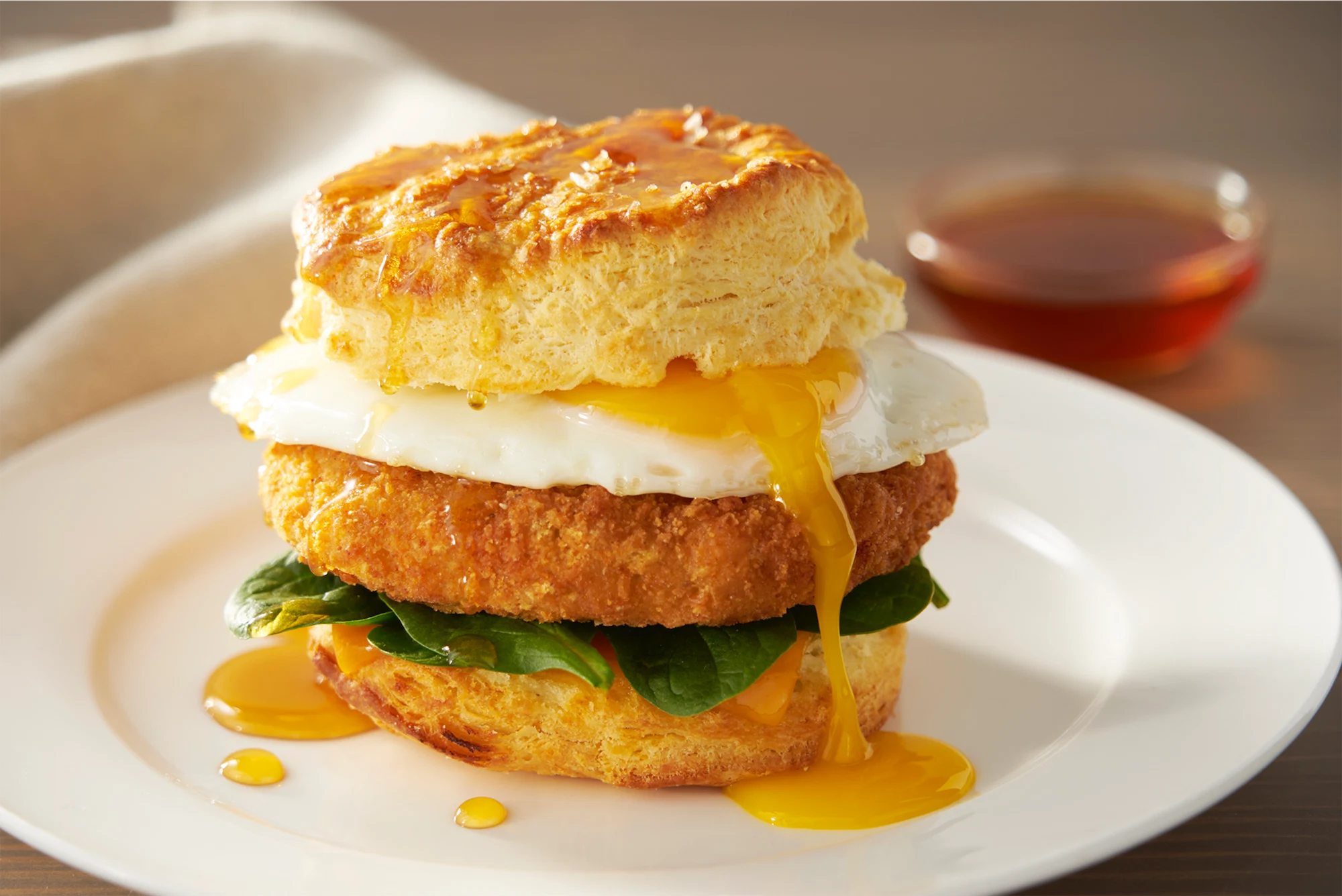 breaded patty fresh baby spinach and a fried egg in a biscuit with yolk dripping down the side on a white plate