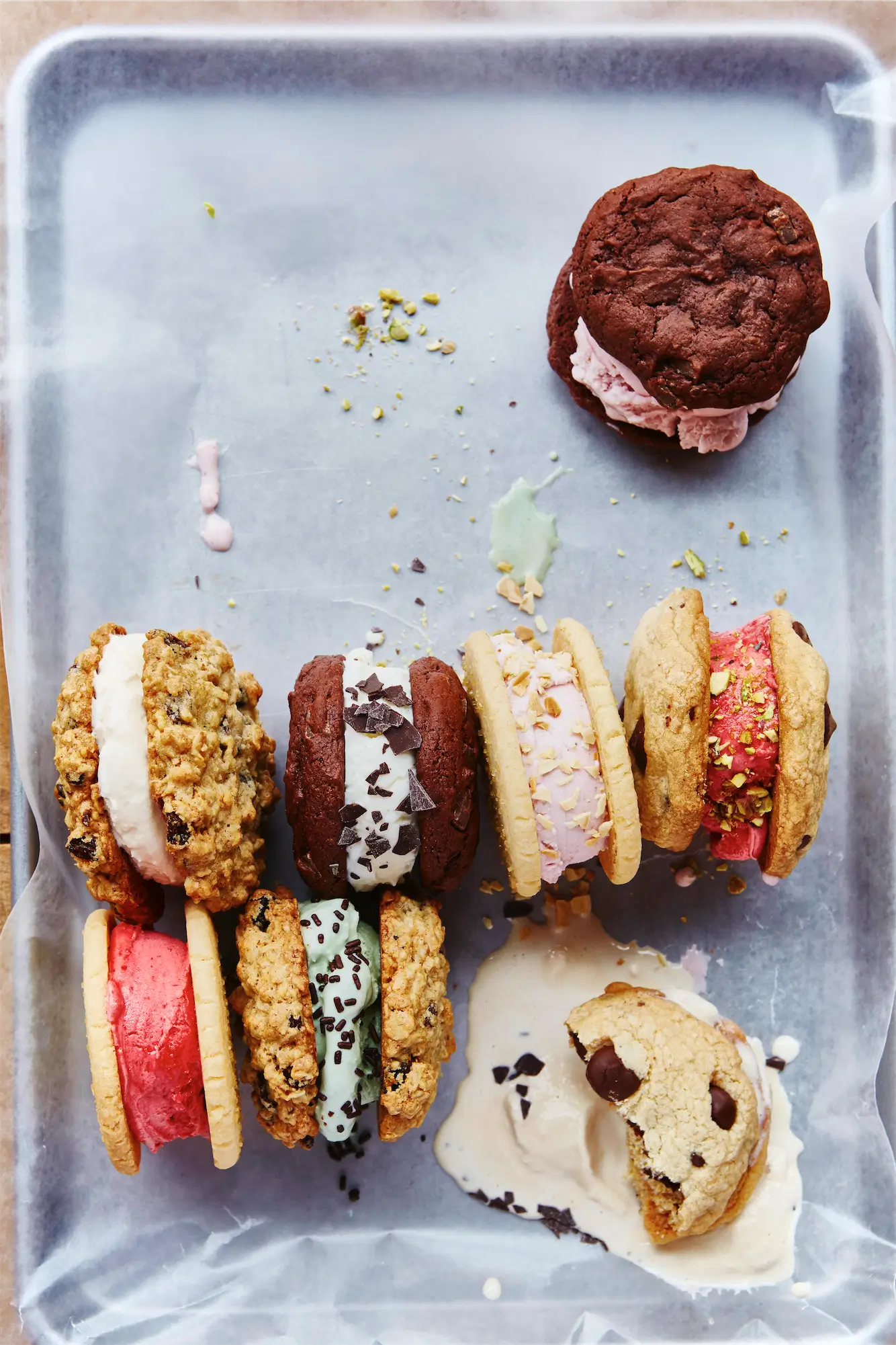 a metal tray of ice cream sandwiches assorted cookies with diffferent color ice creams some are melting