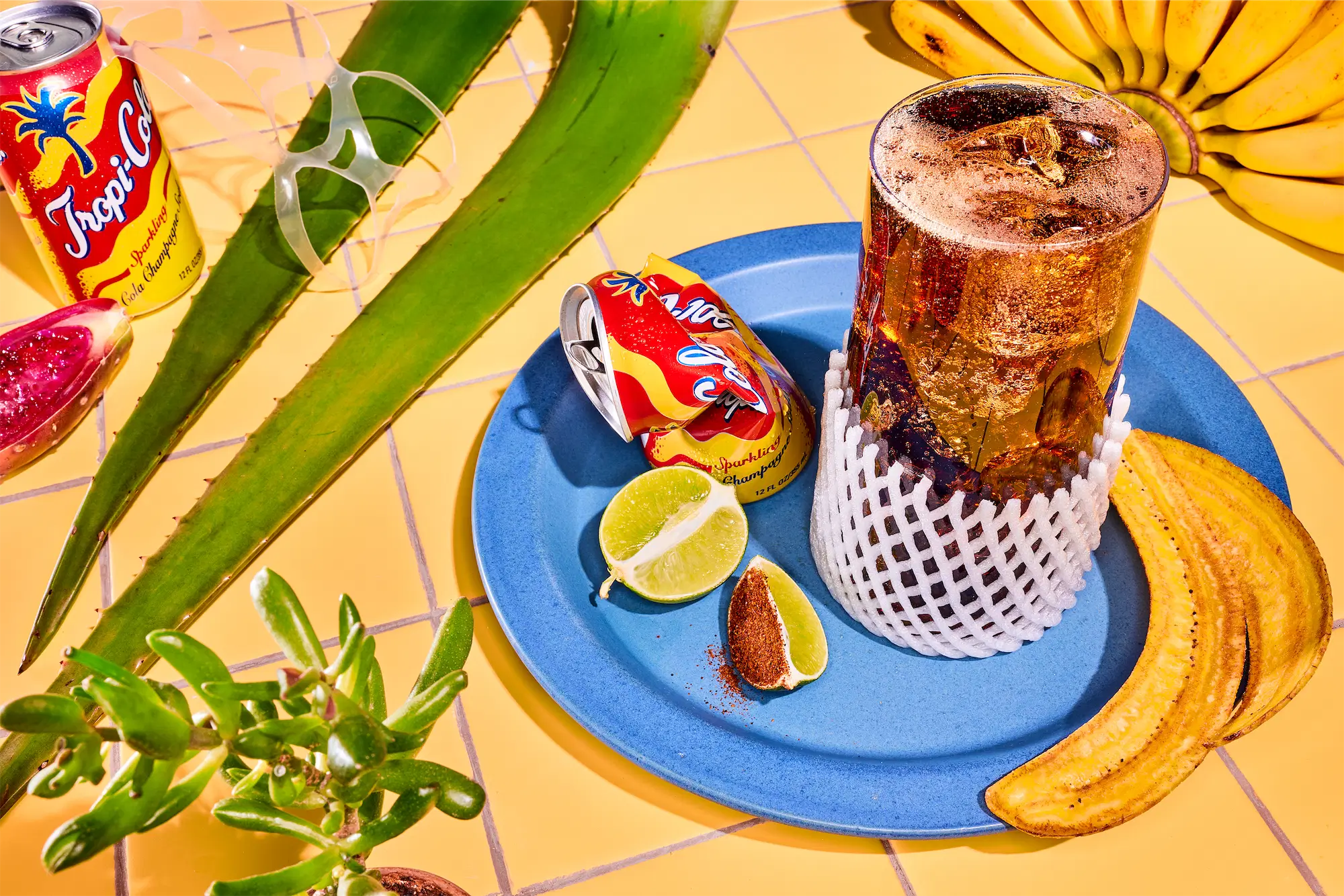 a surreal scene inspired by ai with a glass of fizzy cola on a blue plate with cactus and bananas on a yellow tiled surface
