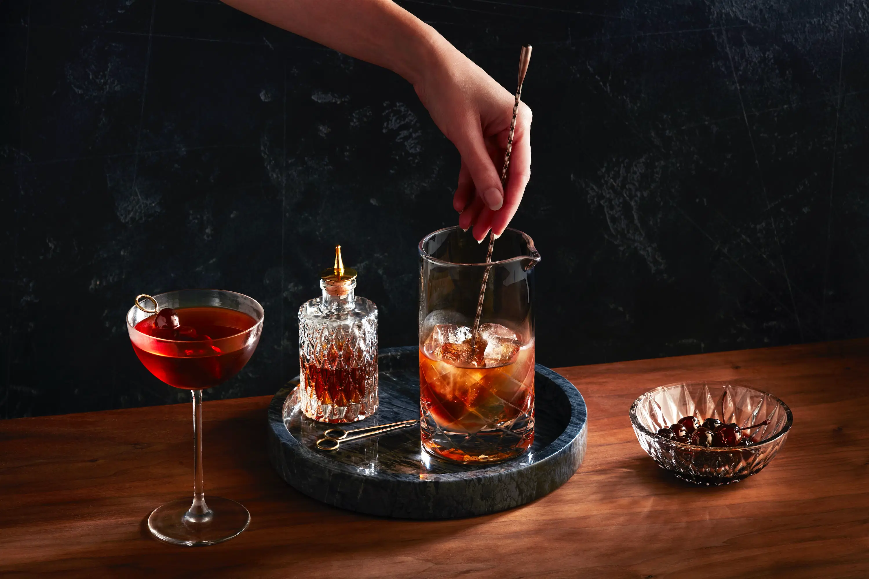 hand stirring manhattan bourbon cocktail in glass pitcher with ice moody scene