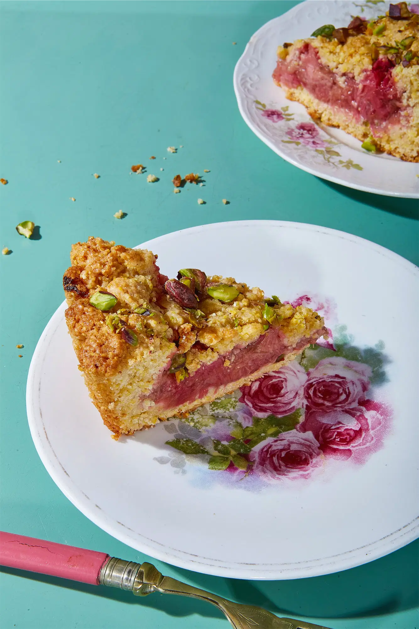 rhubarb almond cake on a floral plate on a turquoise background with a pink fork