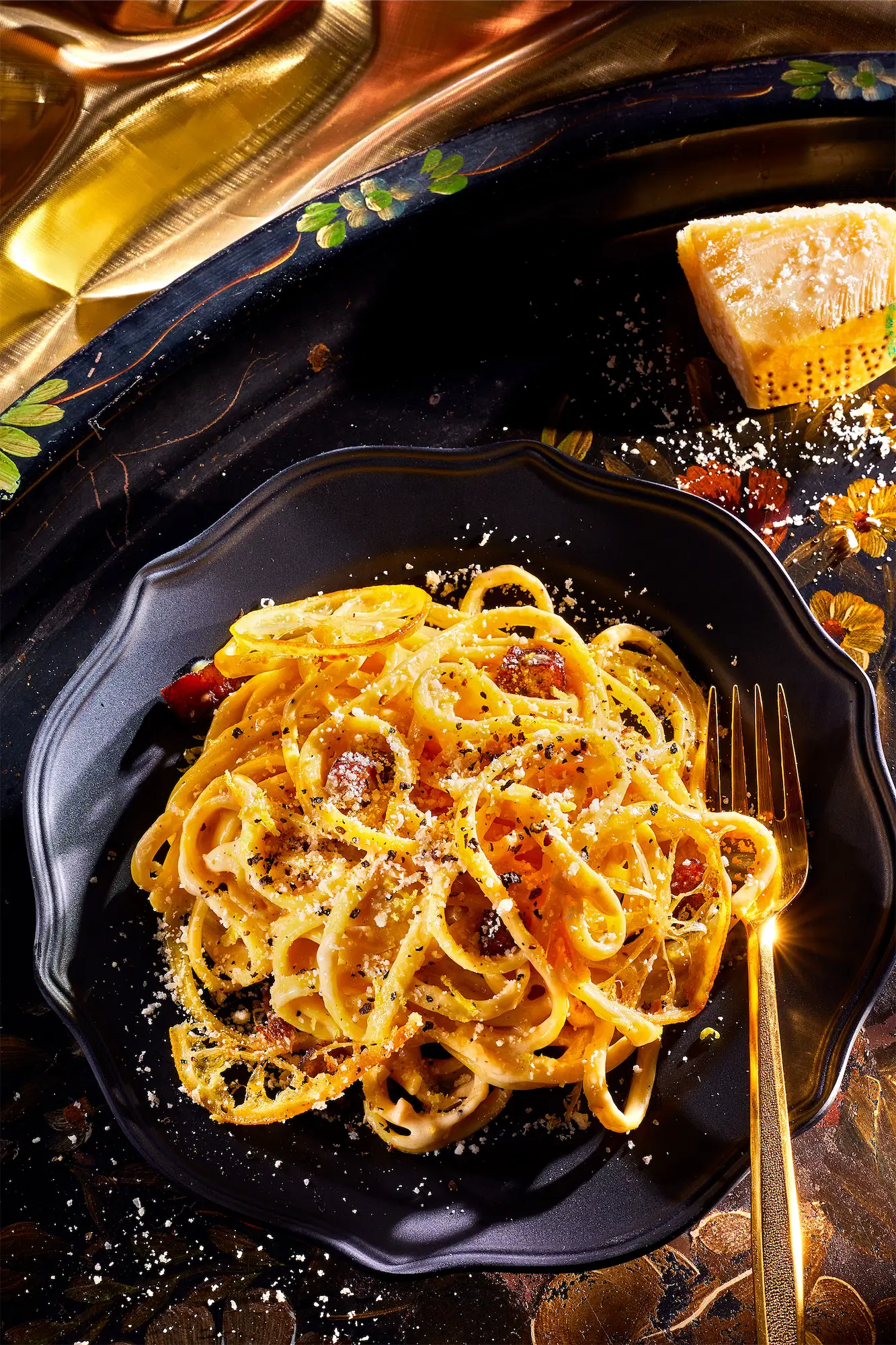 golden yellow italian spaghetti dish with grated parmesan on a black plate with gold fork