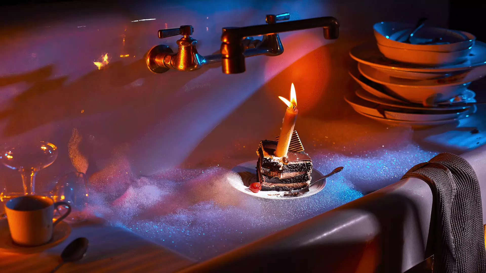 MT2 slice of celebration cake with a flickering candle floats in a sudsy vintage sink with piles of dirty dishes