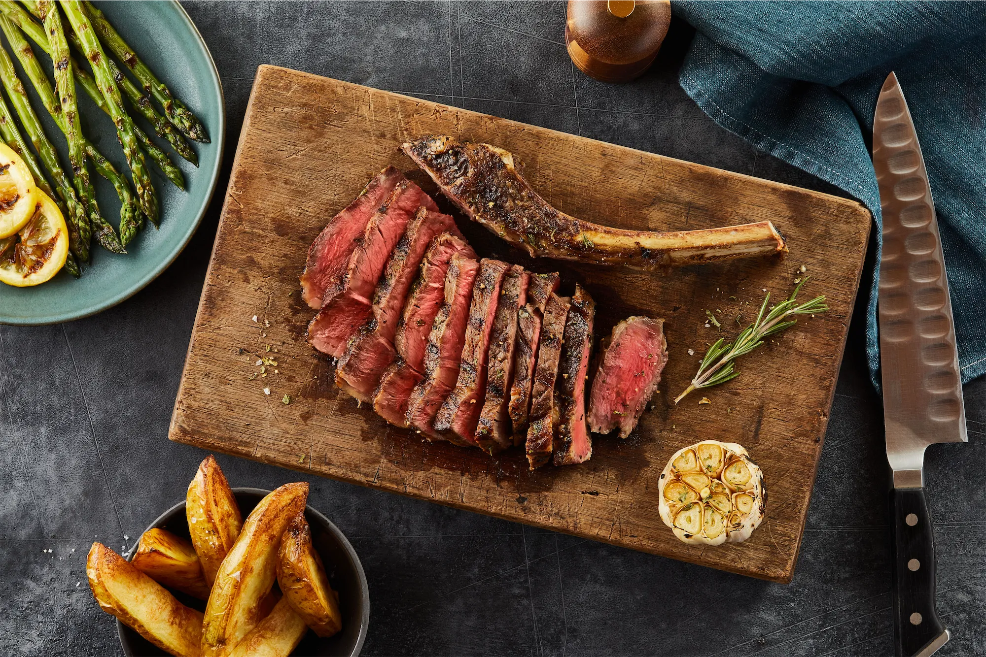 cowboy steak sliced rare on wooden board with french fries and asparagus sides