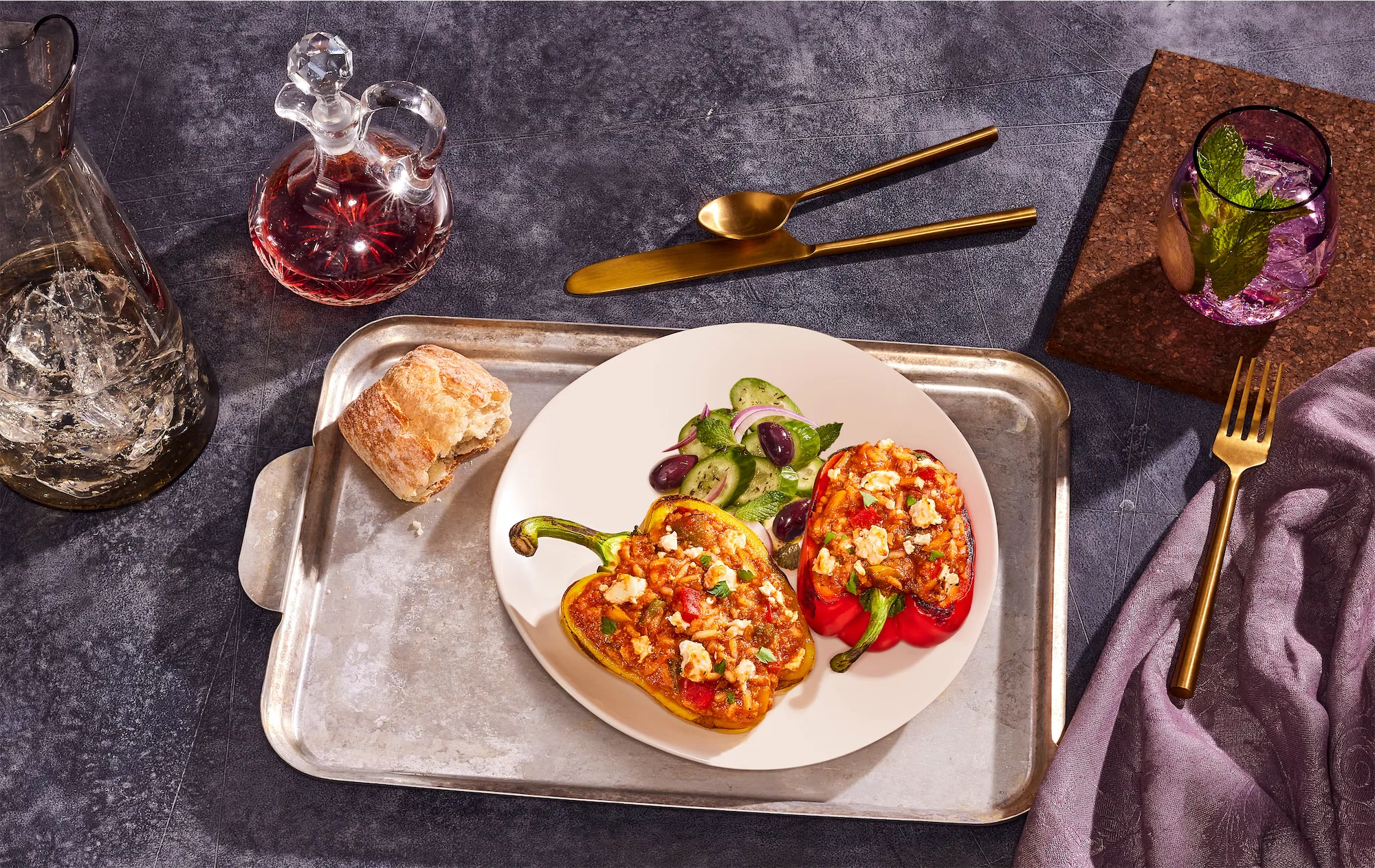 styalized scene of stuffed peppers on a white plate on metal tray with purple accents gold flatware