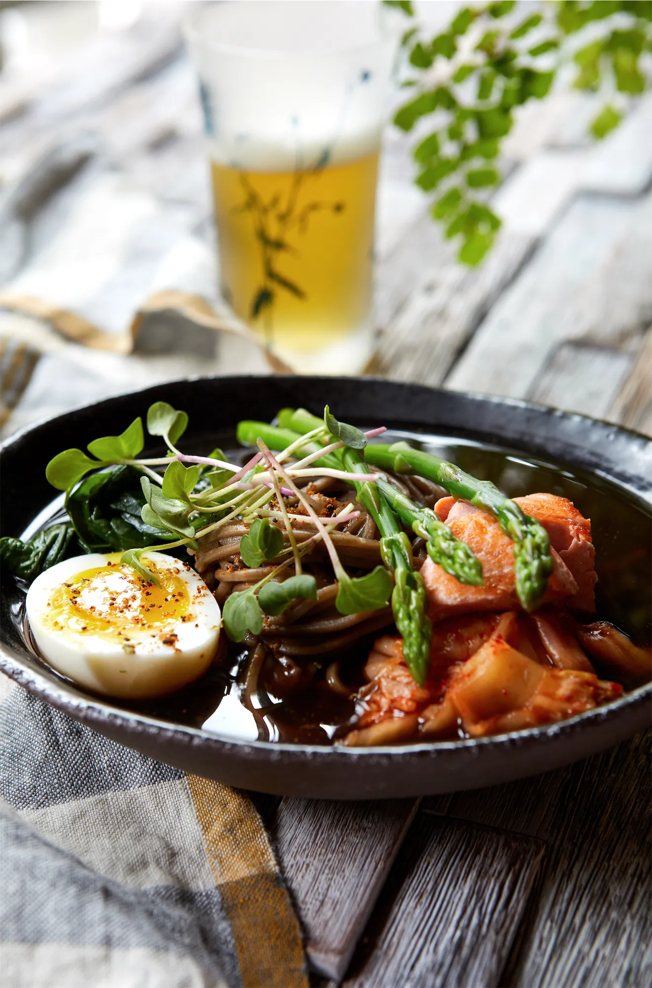 ramen bowl with salmon noodles jammy egg asparagus and sprouts glass of beer on rustic wood surface