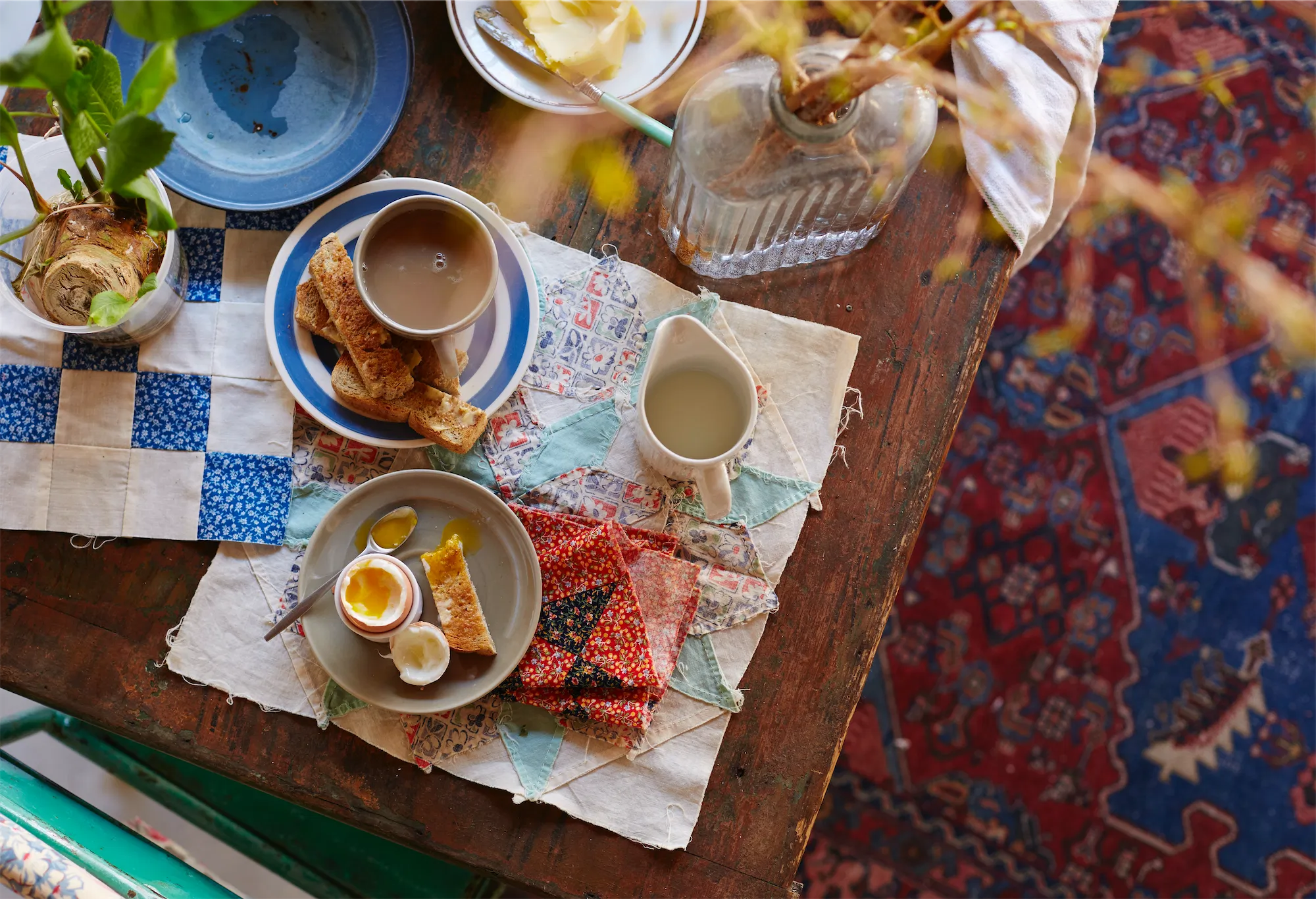 overhead of breakfast table with boiled eggs and toast soldiers cups of english tea folksy patchwork placemats wooden table antique rug