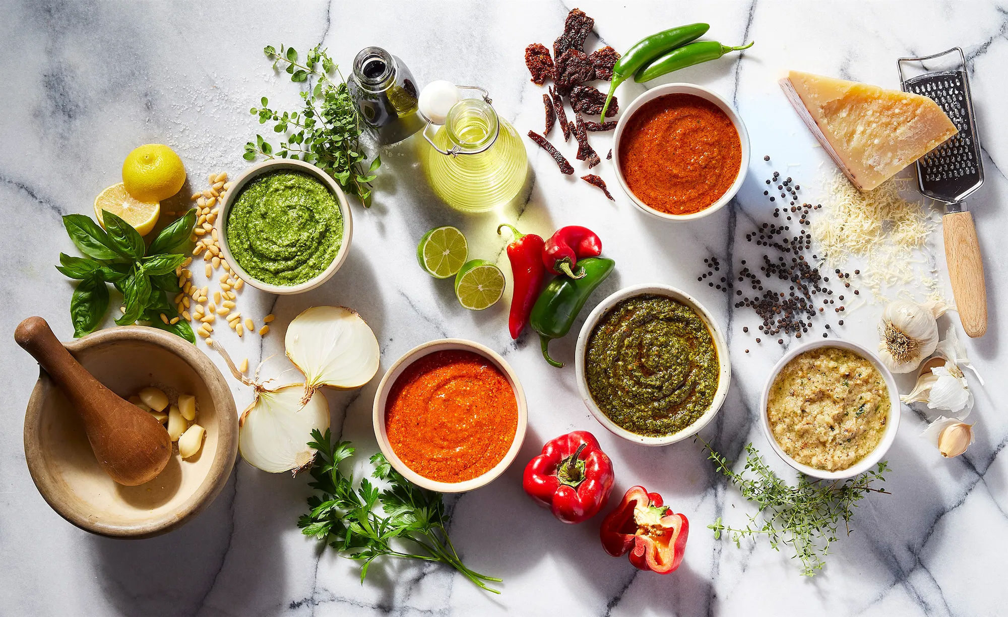 Armenino foods assorted pesto sauces on marbel surface with fresh herbs vegetables olive oil and parmesan