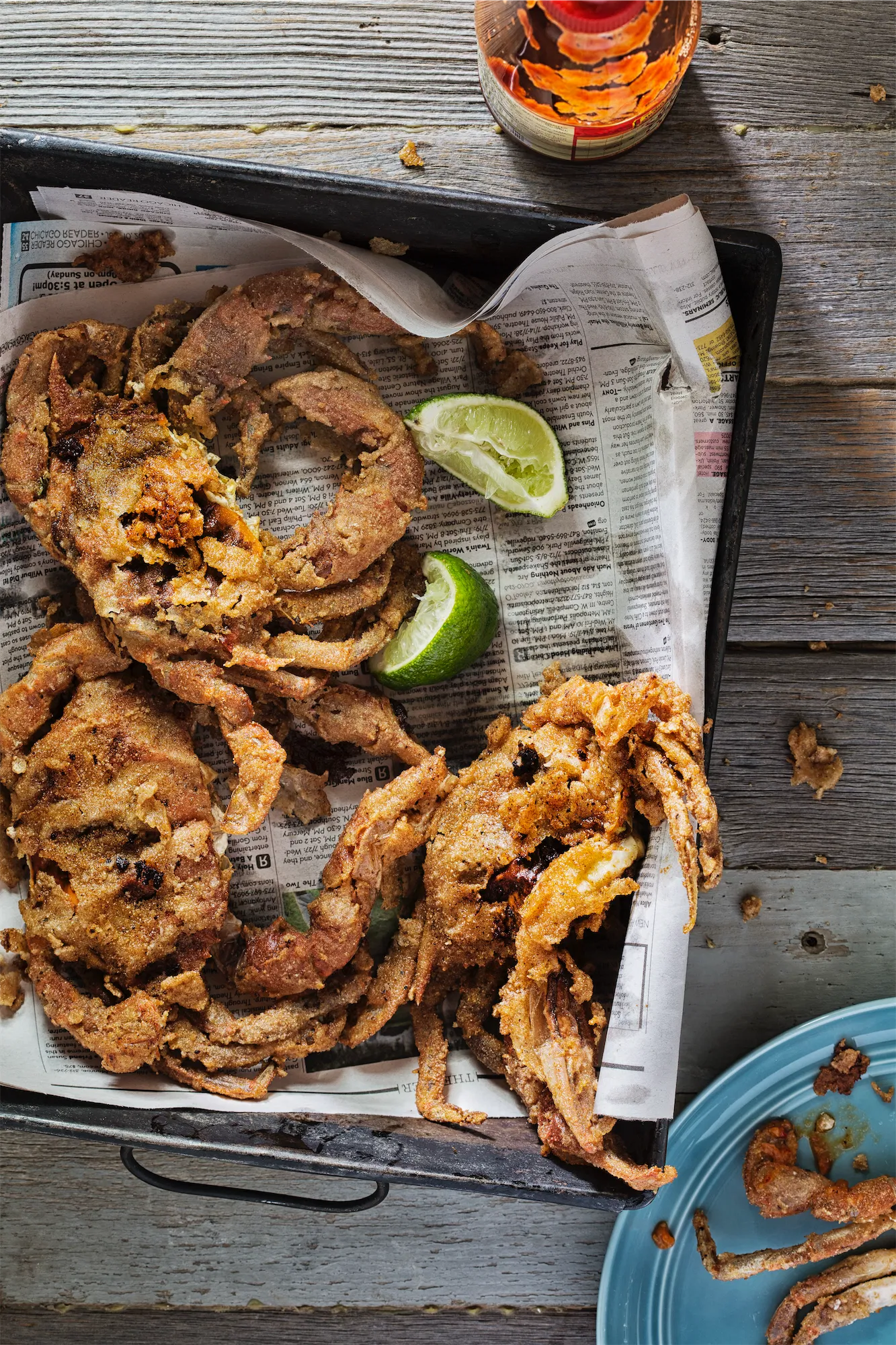 breaded soft shell crab in a newspaper lined tray with lime wedges and a beer bottle