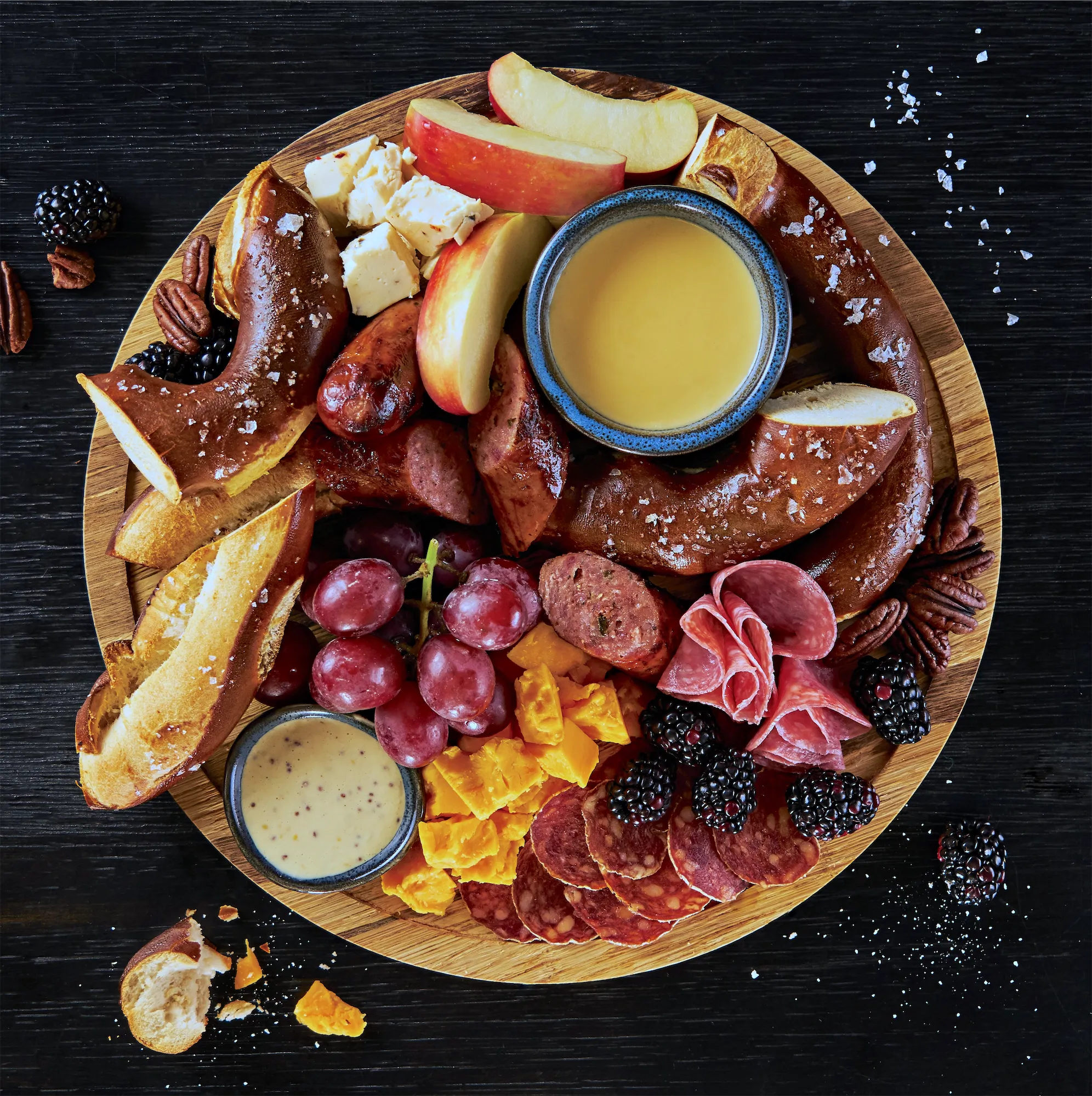 wisconsin style meat and cheese board with pretzels bratwurst salami cheddar apples mustard sauce berries