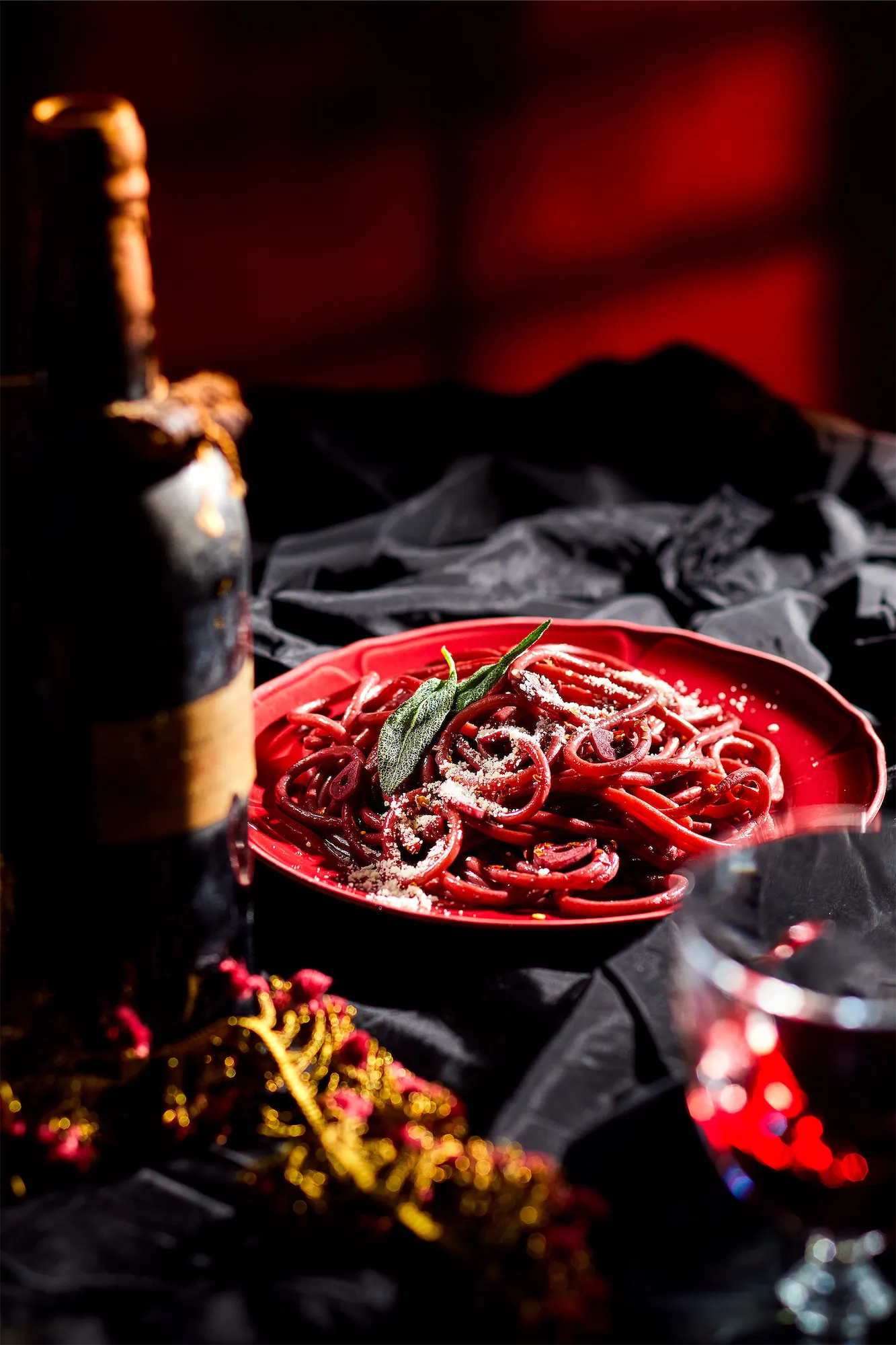 moody scene with red spaghetti on a red plate with a bottle of vintage red wine