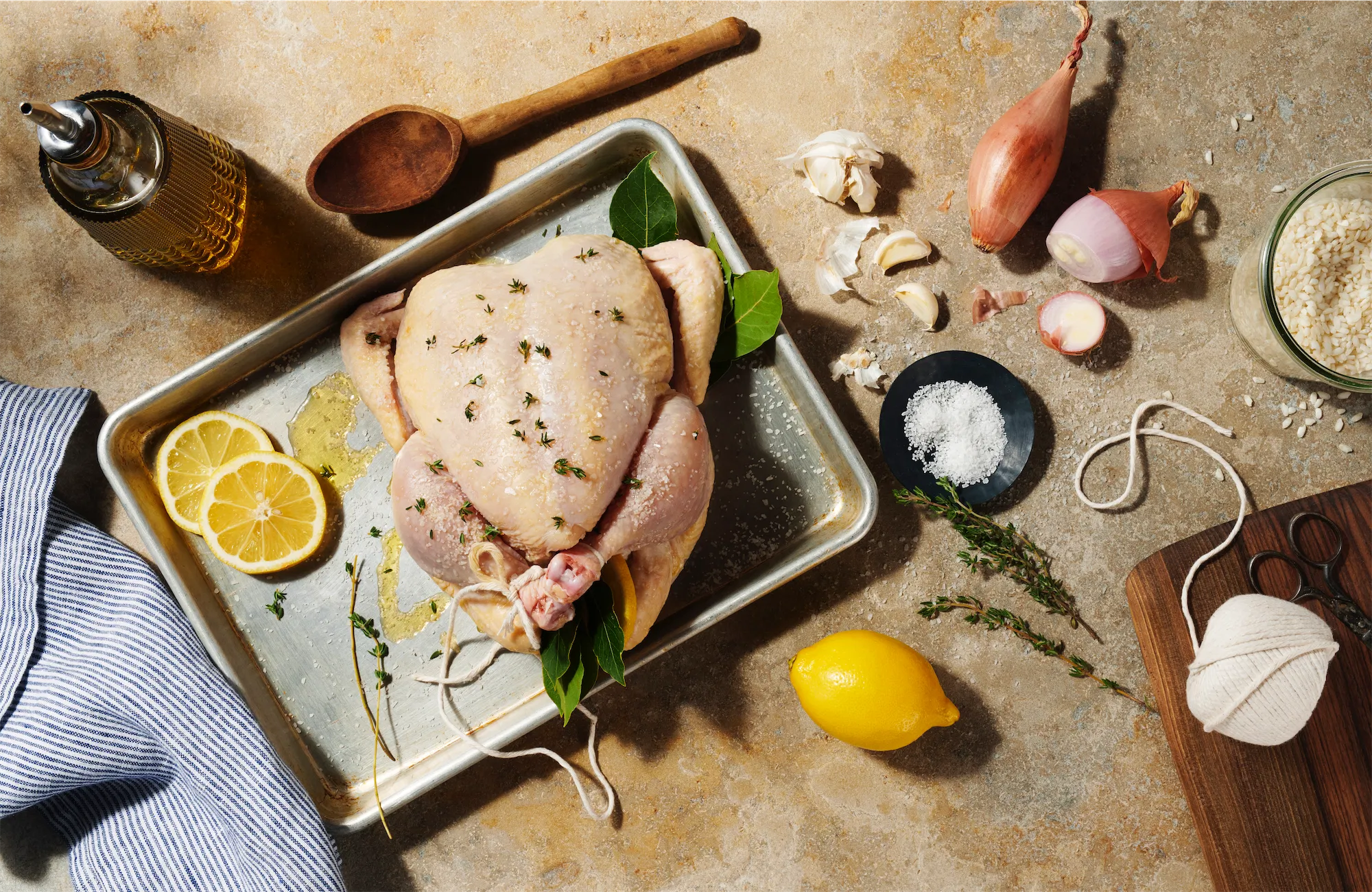 trussed chicken ready to roast on a baking sheet with shallots lemons bay leaves salt and garlic