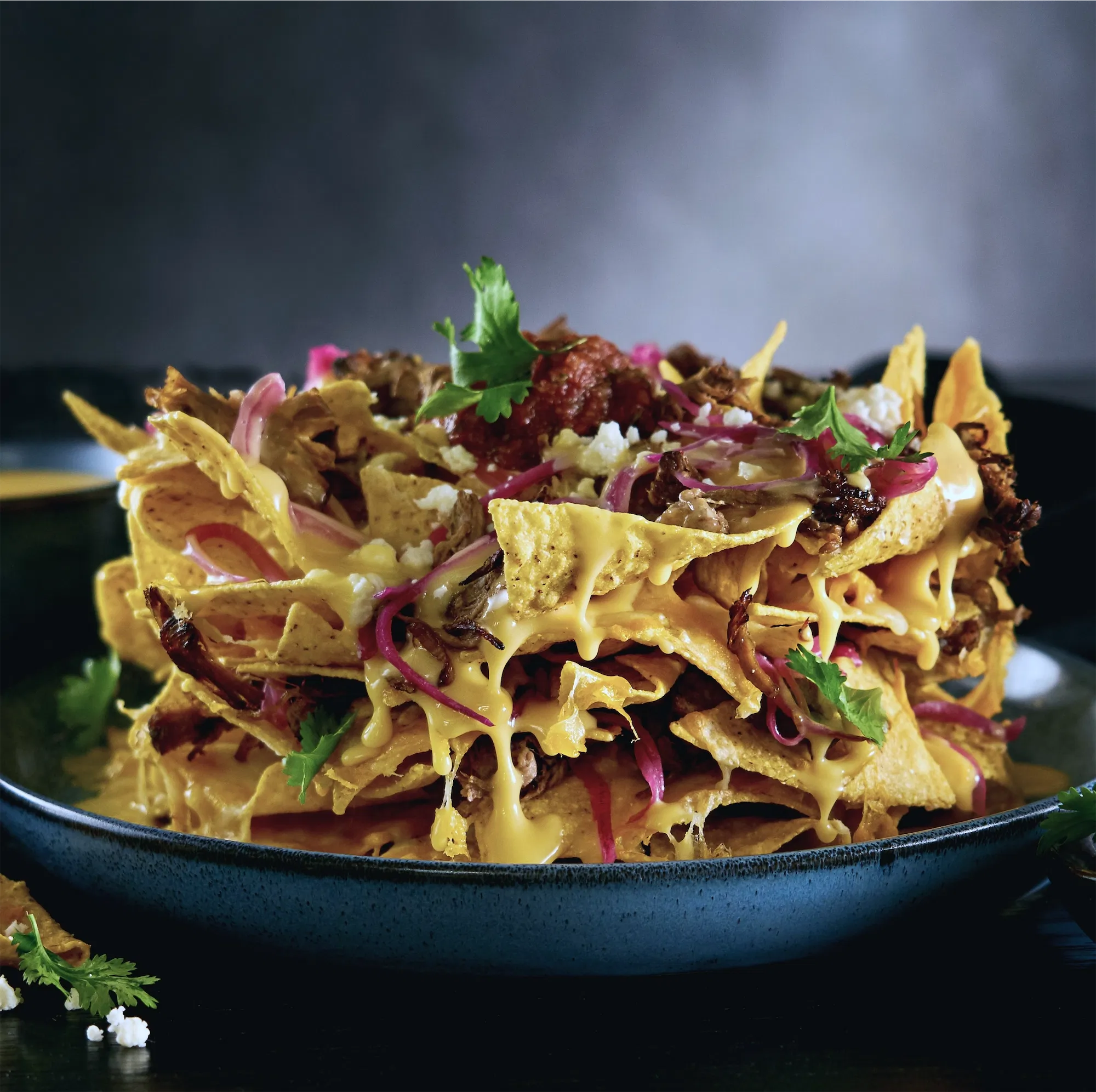 Pile of gooey cheesy nachos on blue plate