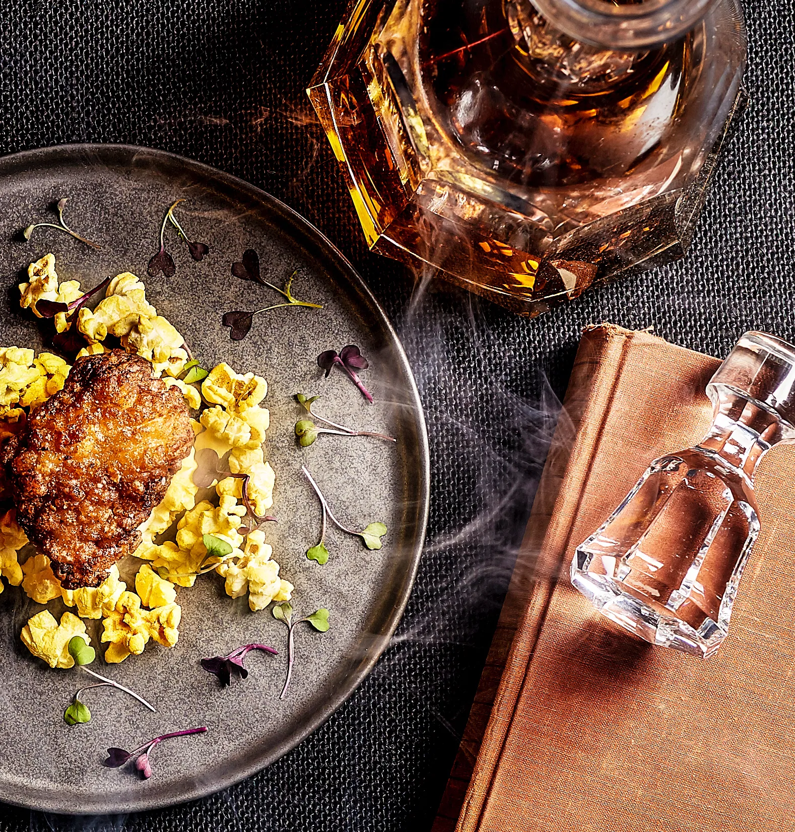 decanter of whiskey beside a plate of popcorn chicken smoke trails