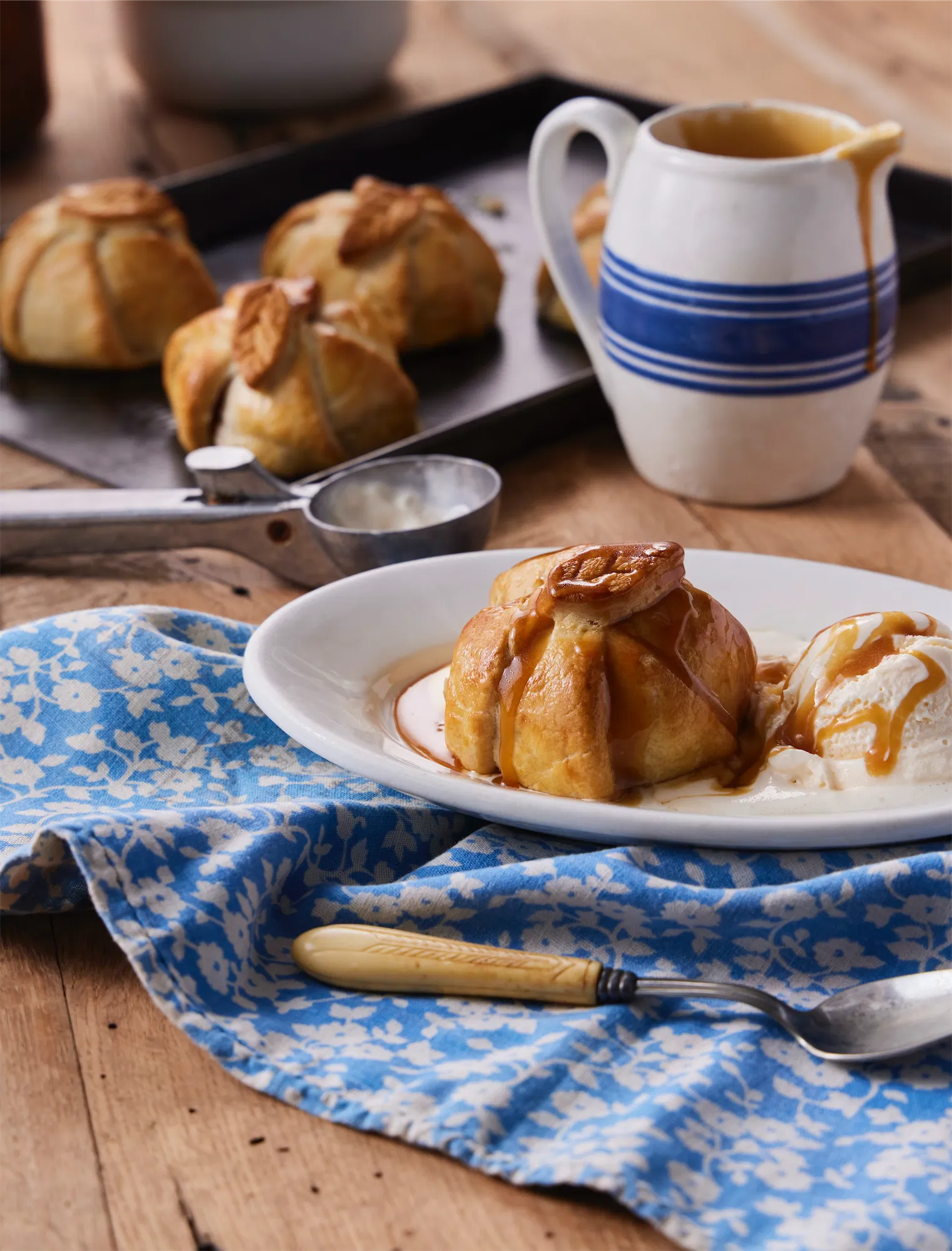 baked apple in puff pastry on a blue and white linen with pitcher in background.