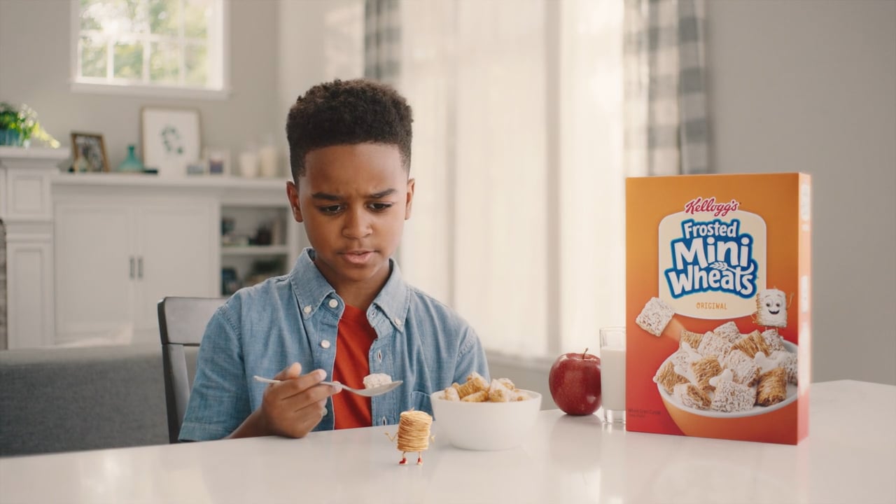 Kellogs frosted mini wheats in a bowl of milk showing animated cartoon character interacting with young african american boy at breakfast