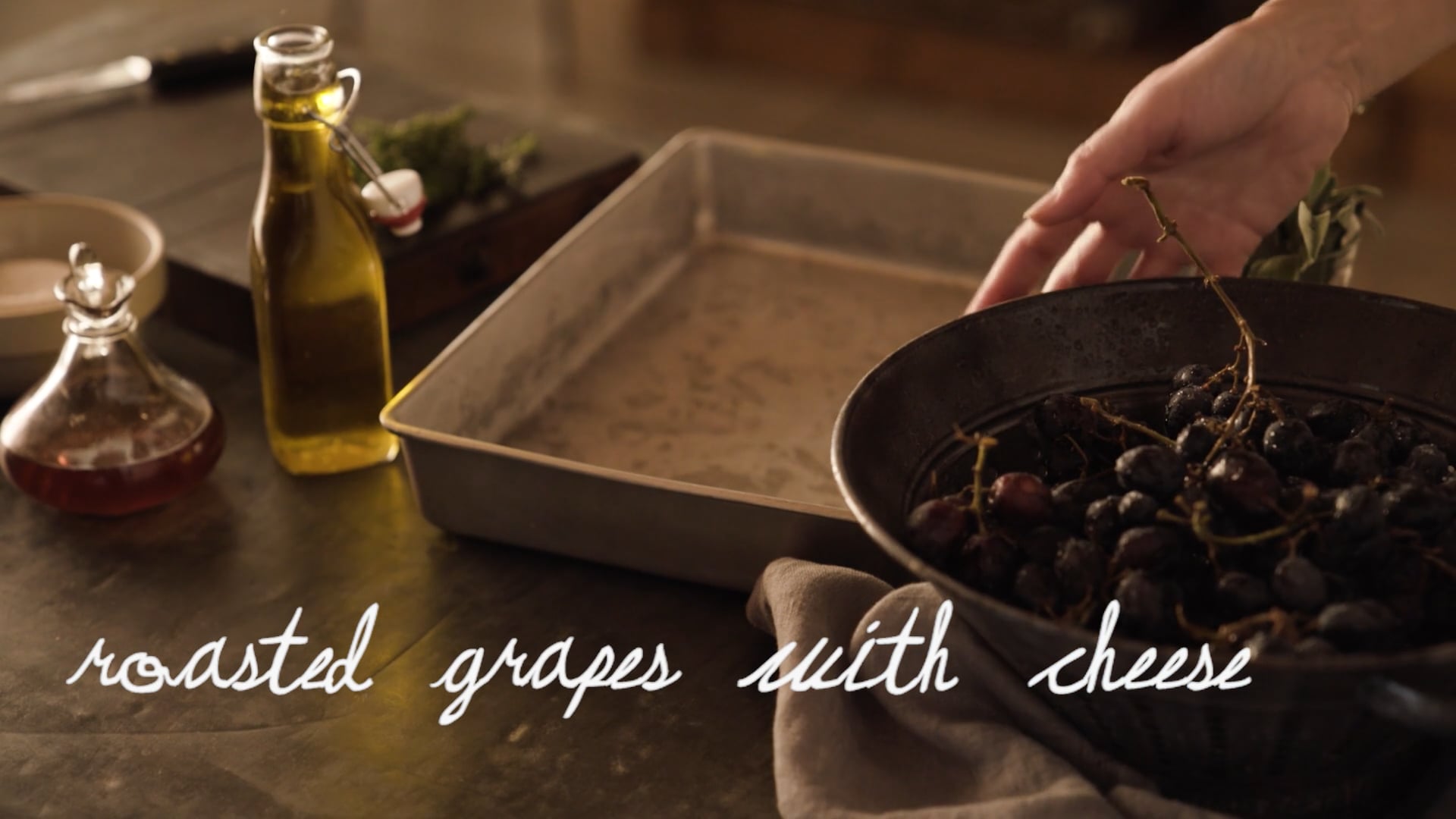 in a romantic european style kitchen with a woman in an apron preparing roasted grapes with soft cheese and thyme mulled wine and soda bread rolls