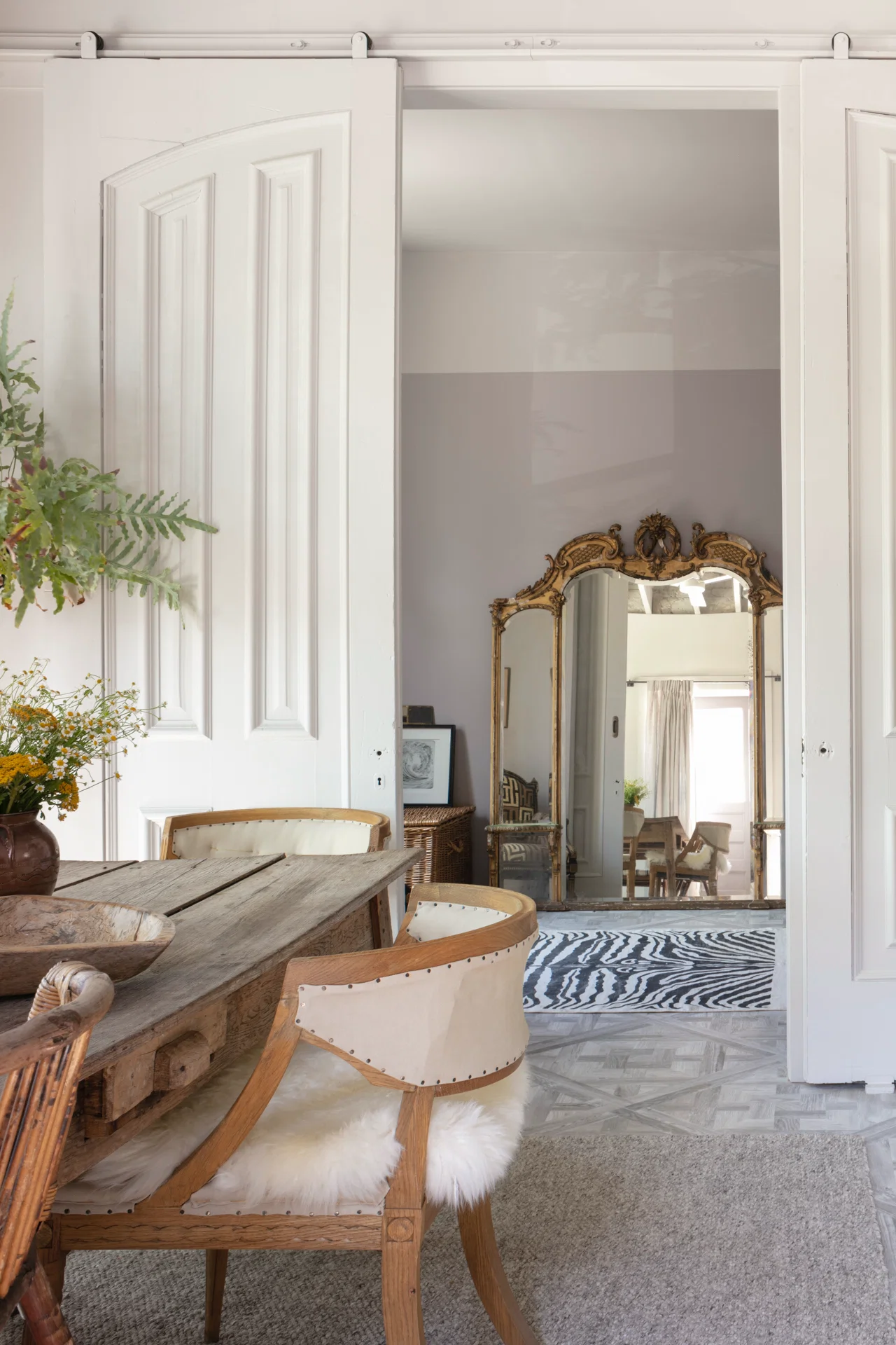 interior scene with oversized vintage rollling door large gilt framed antique mirror wooden dining table restoration hardware upholstered dining chairs