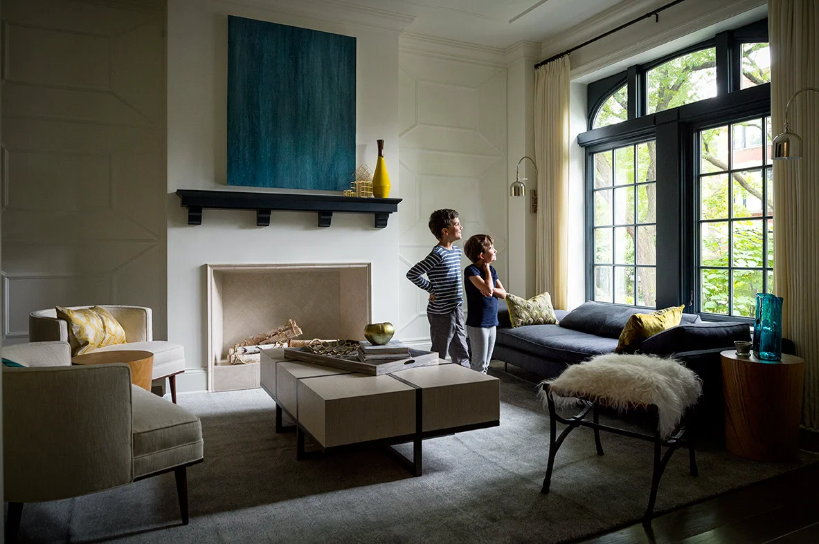 Chicago magazine upscale large living room with sofa and coffee table large artwork over fireplace and two young boys looking out of oversized window