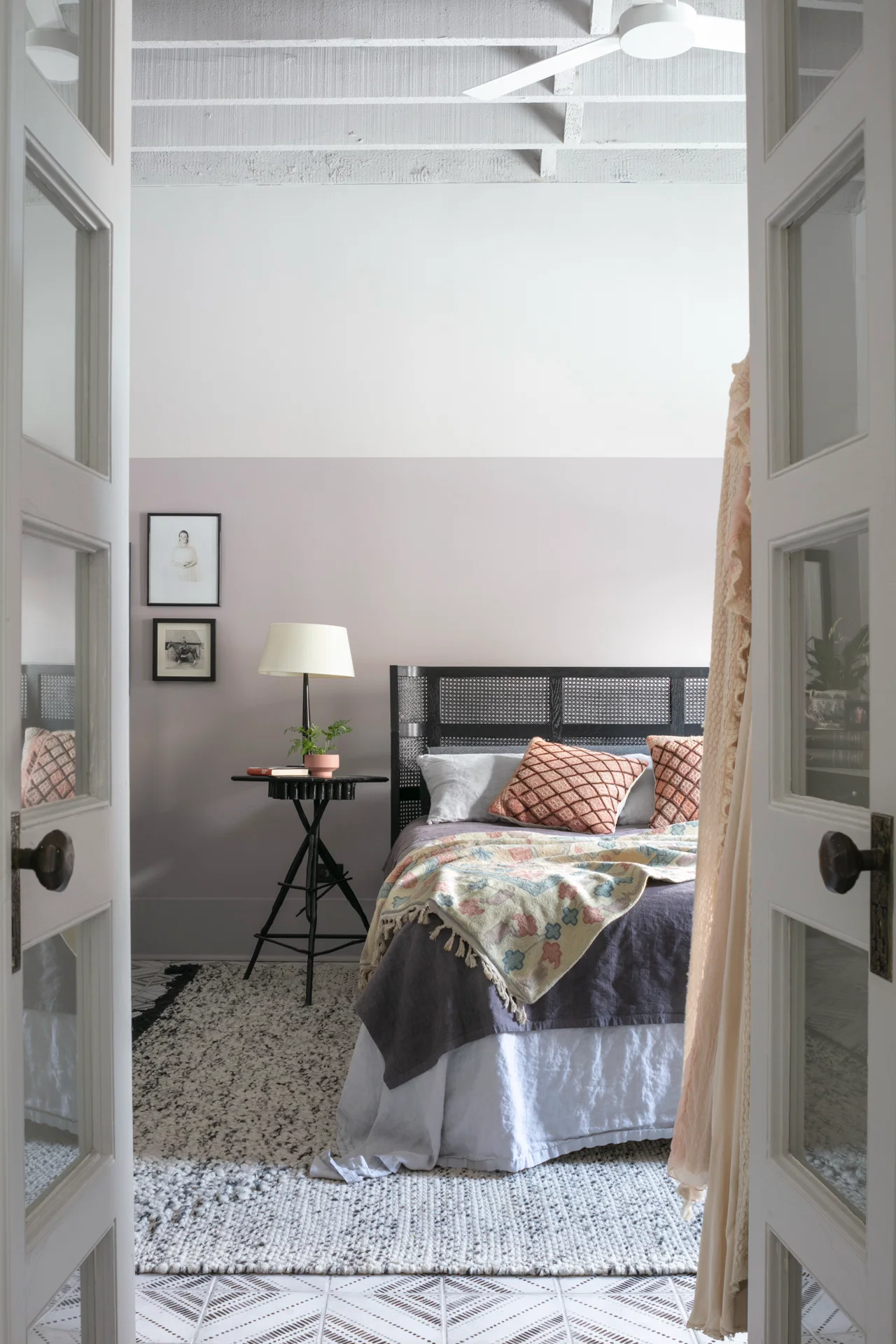 interior bedroom scene cb2 rattan bedframe nightstand grey two tone wall french doors