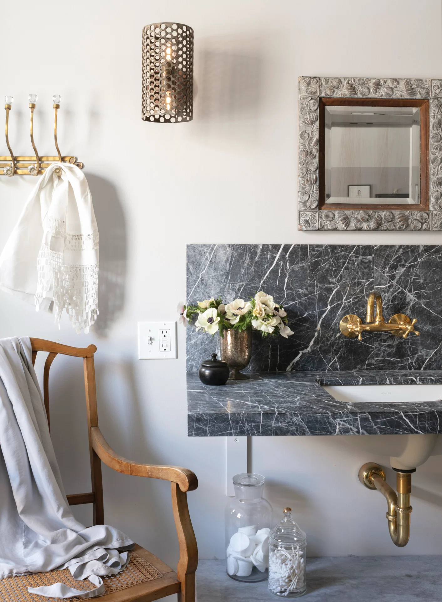 interior bathroom grey marble sink antique wood chair brass towel hooks metal wall sconce